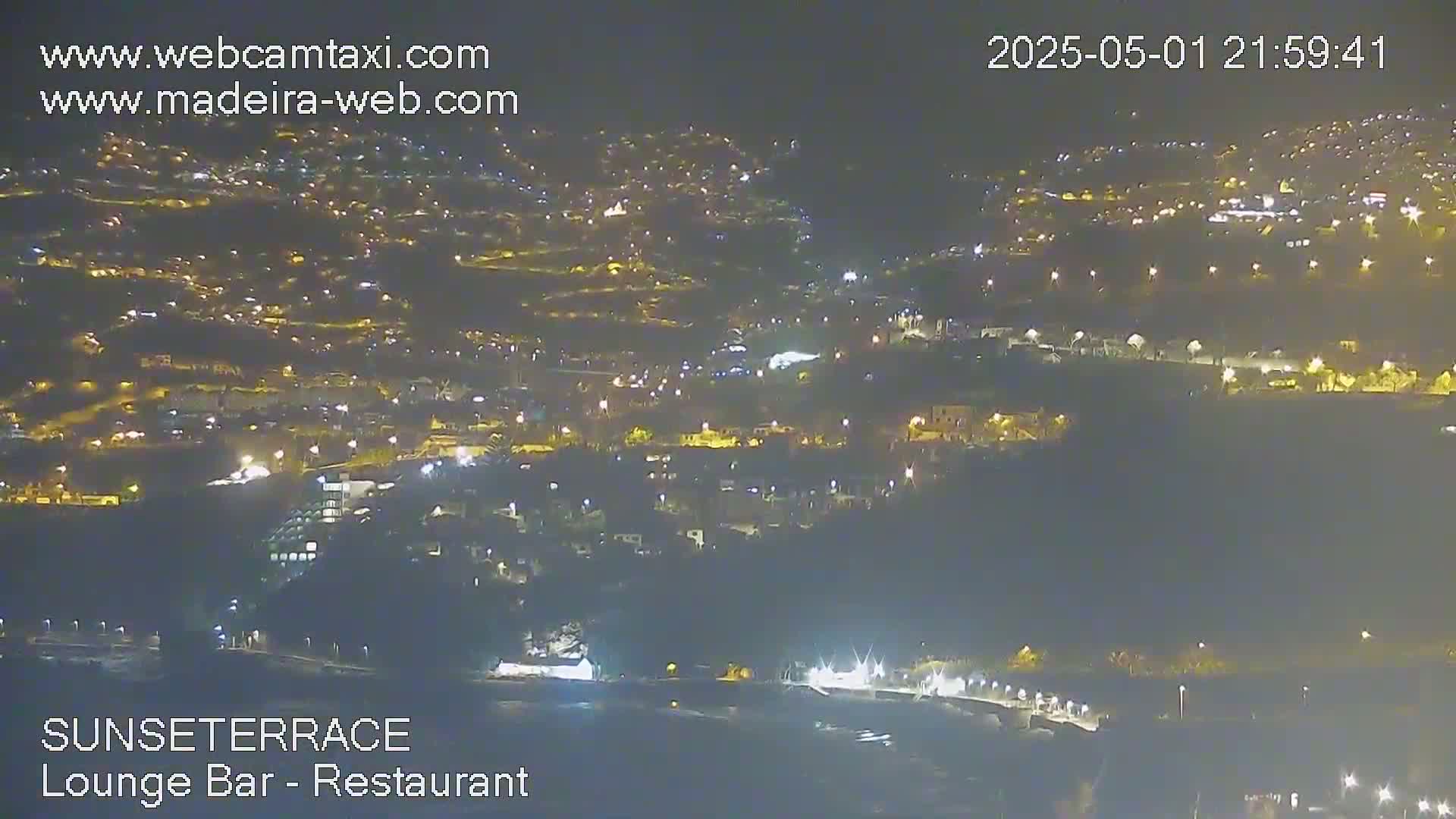 A nighttime, aerial view of a town illuminated by streetlights, with a dark body of water visible in the foreground.