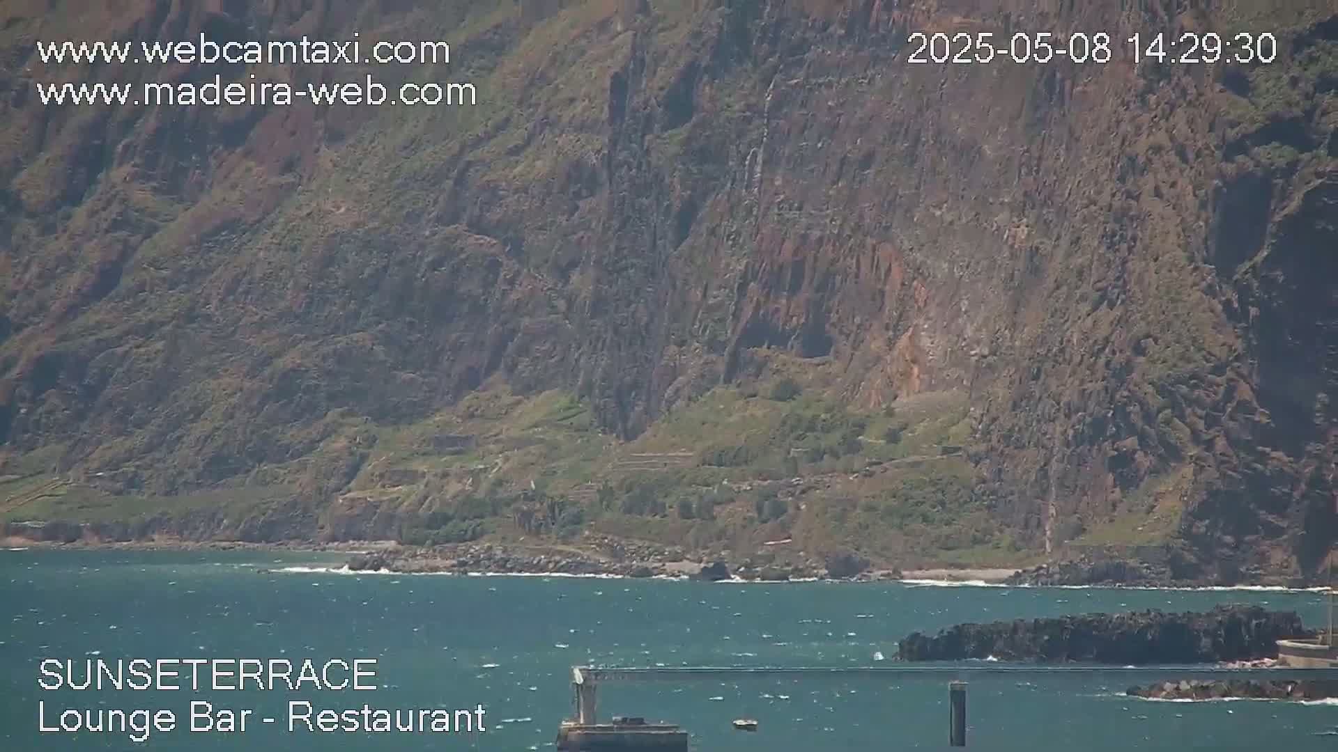 A rocky cliffside overlooks a body of water with small waves under a partly sunny sky.