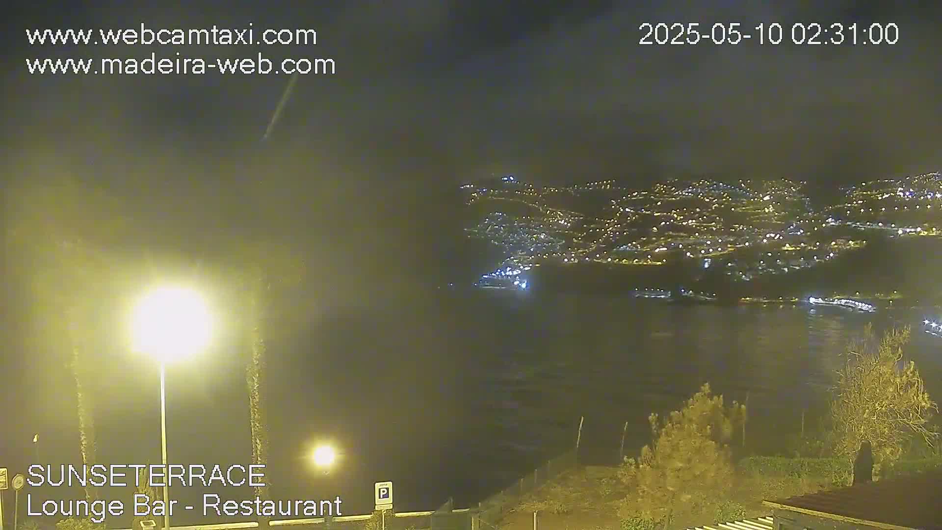 A nighttime view of a city lights spread across a hillside, partially obscured by hazy weather, seen from an elevated vantage point.