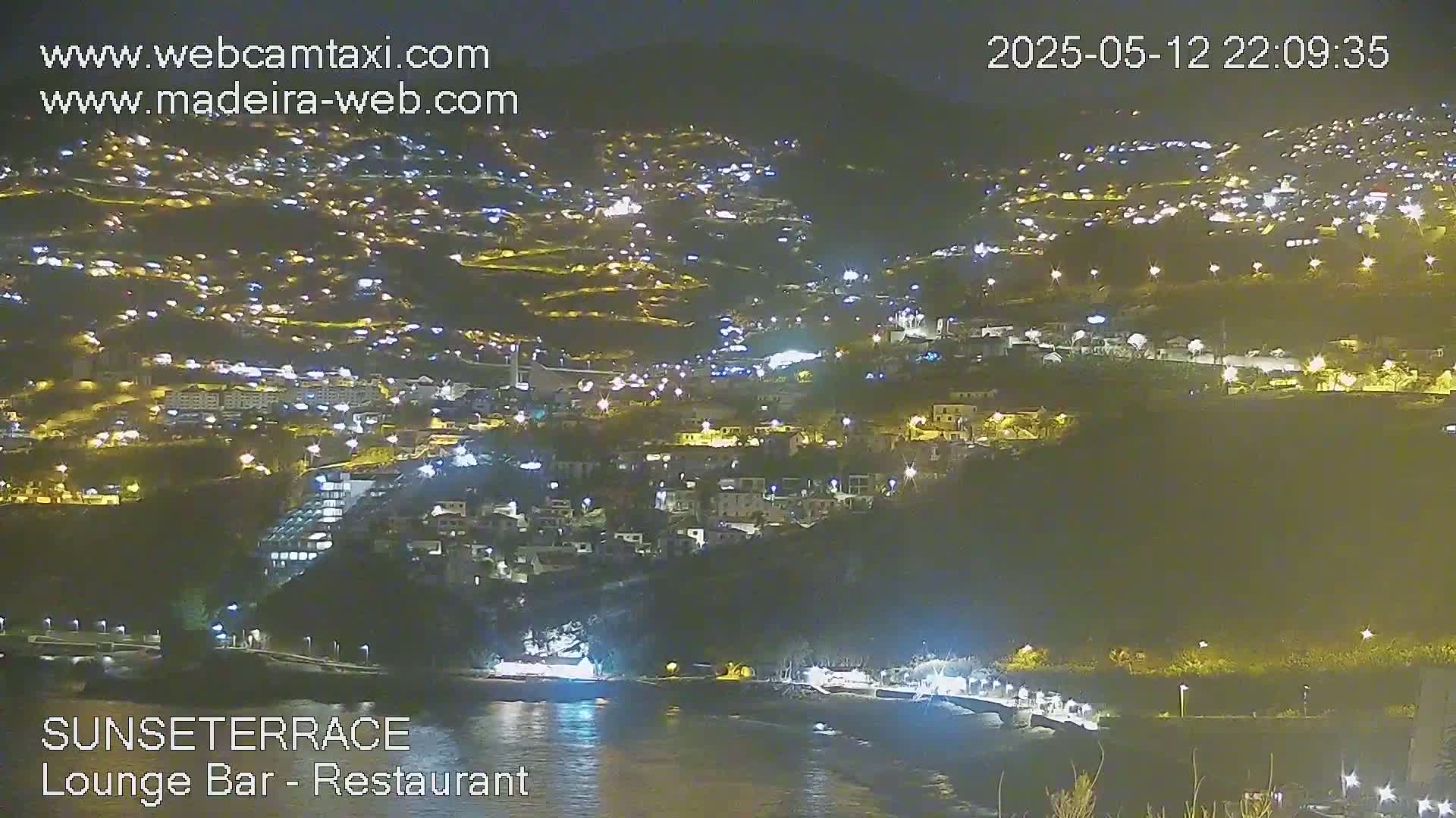 A nighttime view of a coastal town illuminated by streetlights, overlooking a dark body of water.