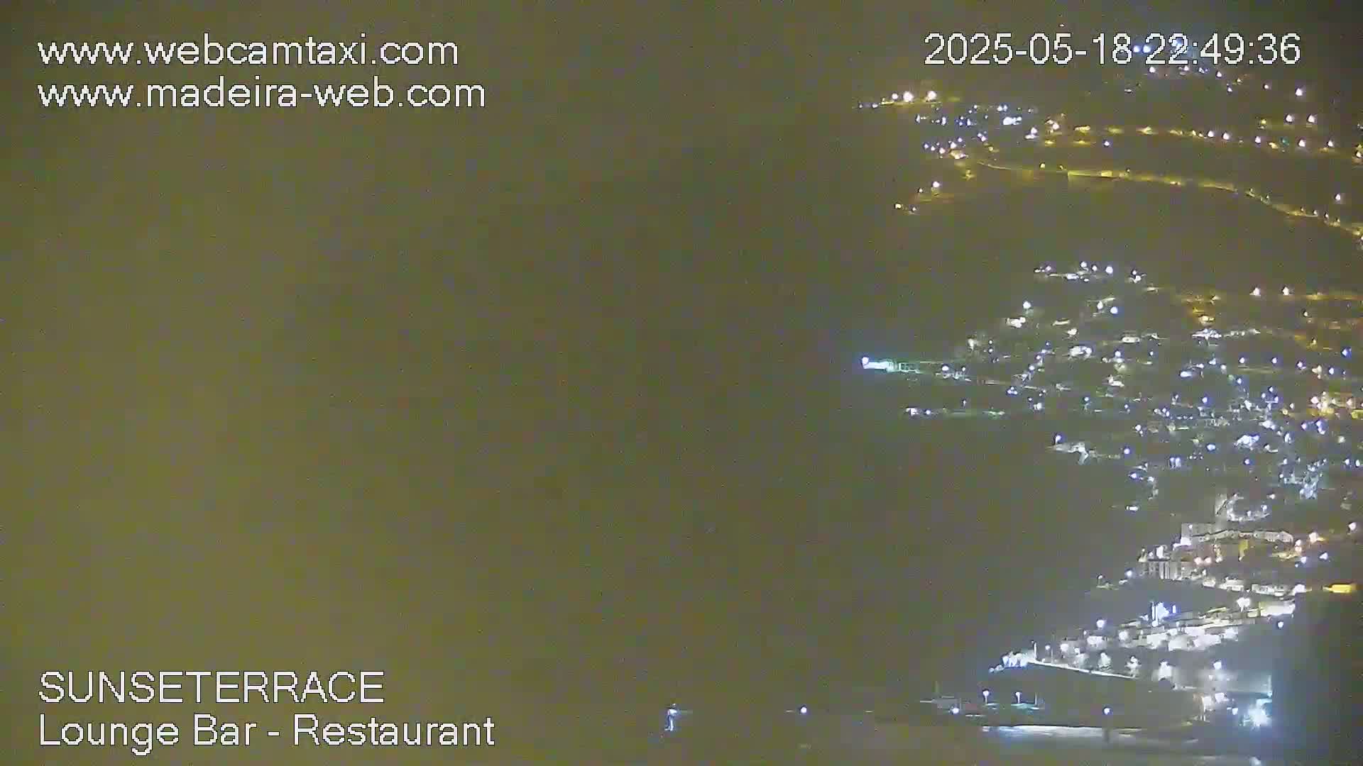A nighttime, long shot of a hillside town illuminated by many lights.