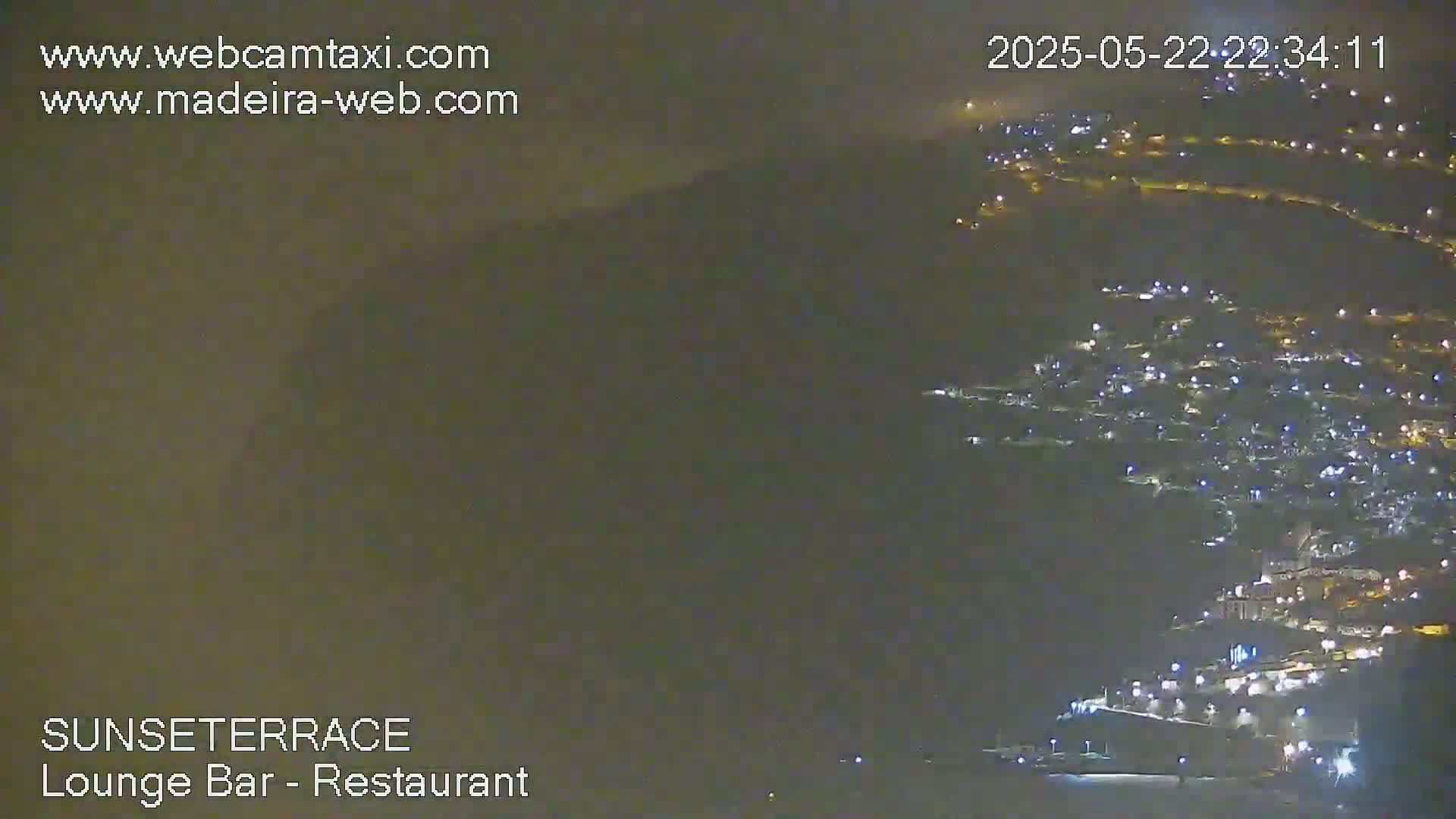 A nighttime, hazy view of a town nestled on a hillside, illuminated by numerous lights.