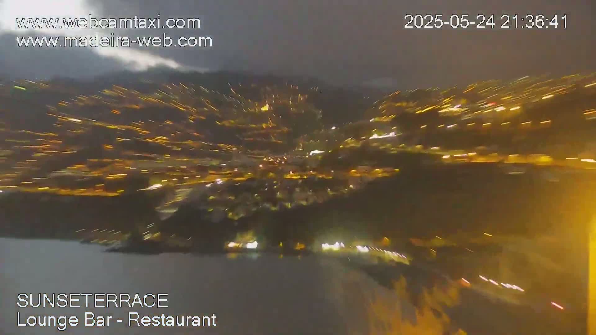 A nighttime, blurry view of a city illuminated by many lights under a dark, cloudy sky.