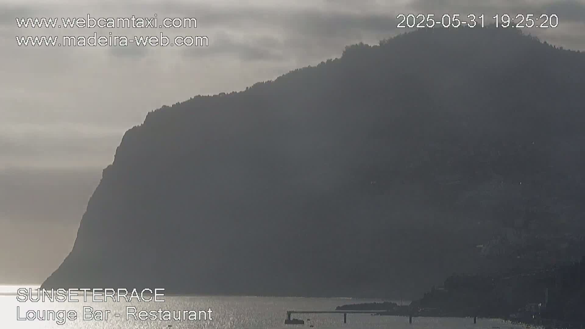 A large, dark mountain looms over a calm body of water under an overcast sky.