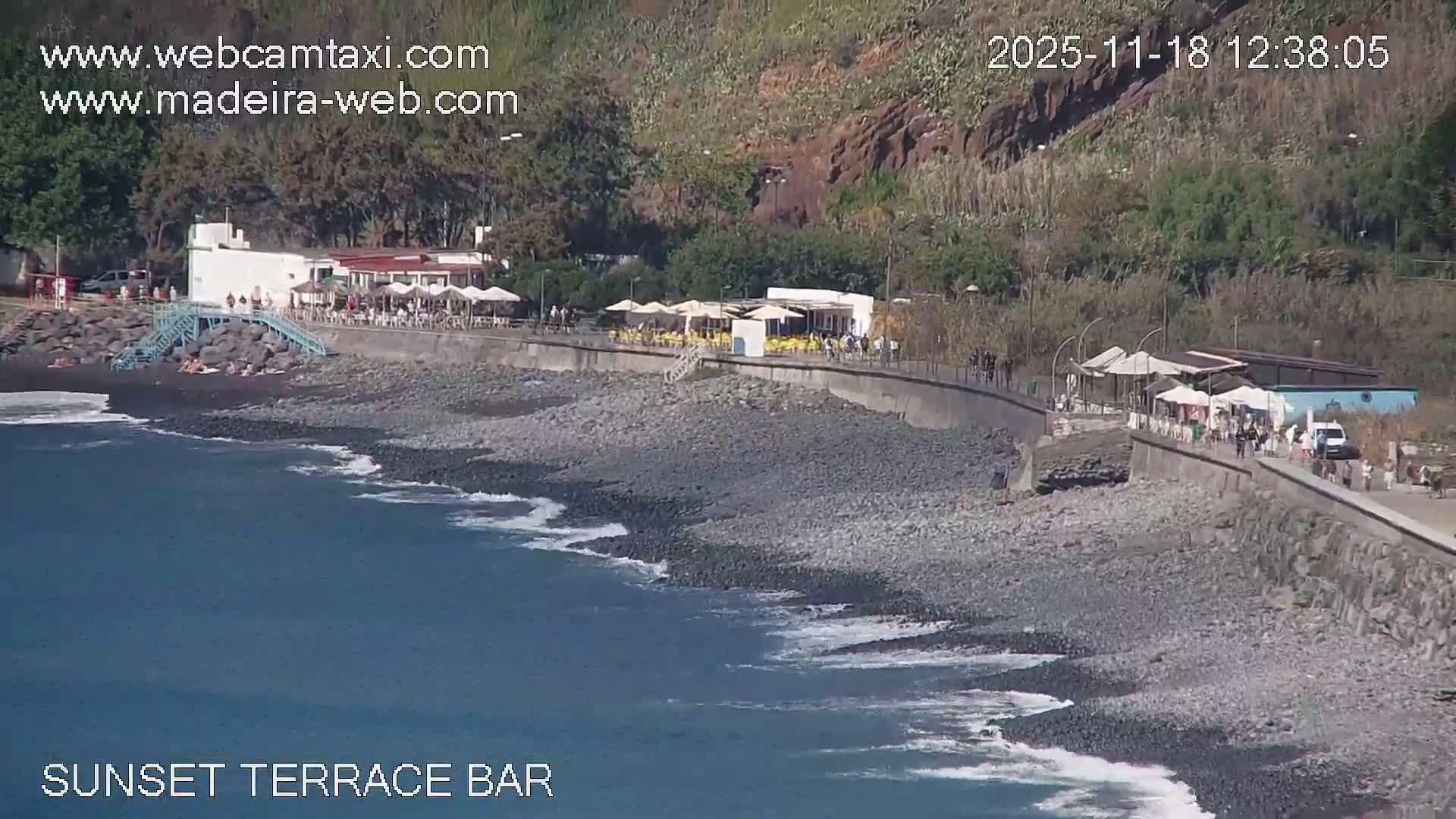A nighttime view shows a hillside town illuminated by lights, extending down to a dark body of water with a brightly lit waterfront.