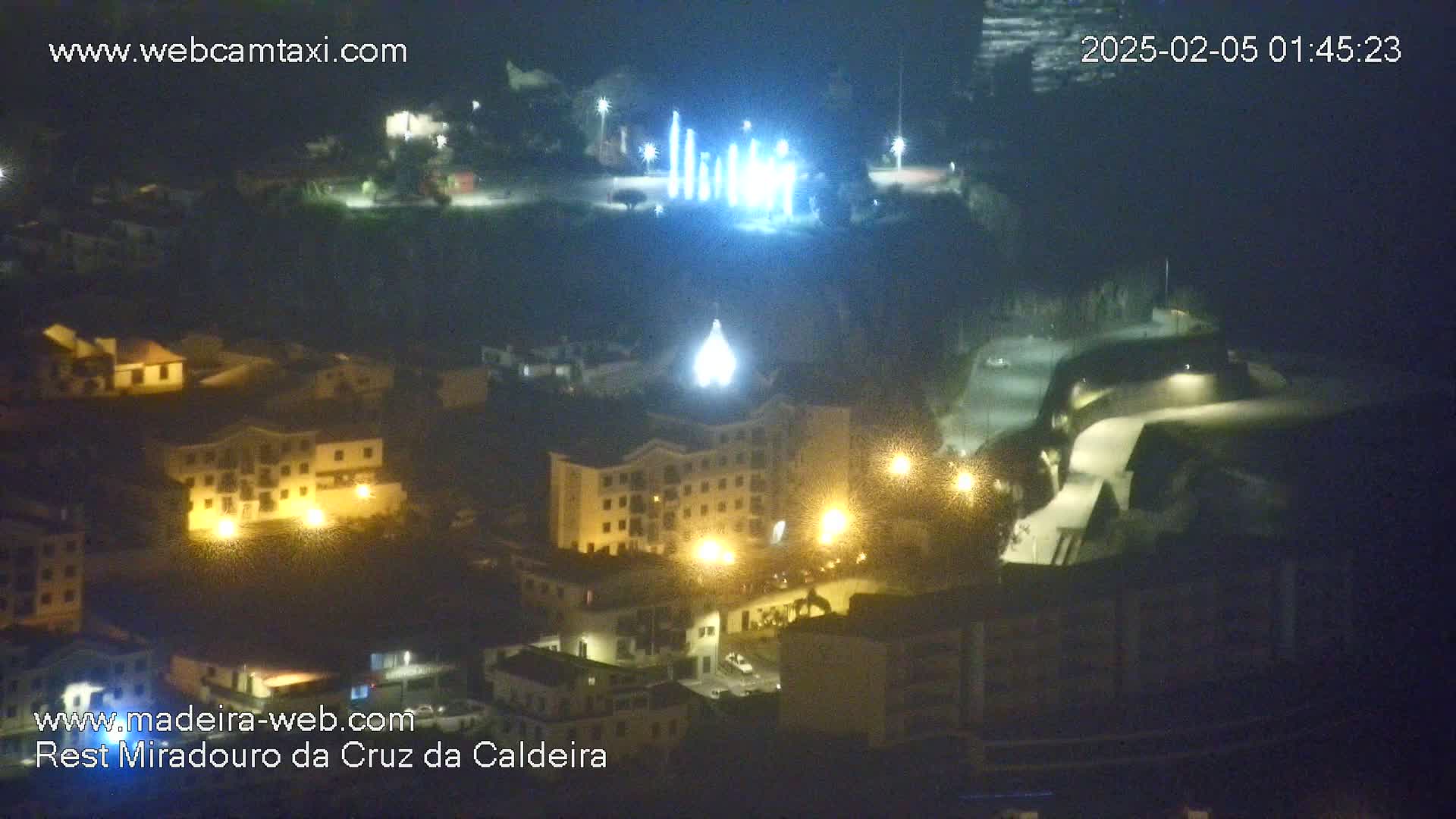 A nighttime, aerial view of a town with illuminated buildings and streetlights, featuring a brightly lit structure in the background.