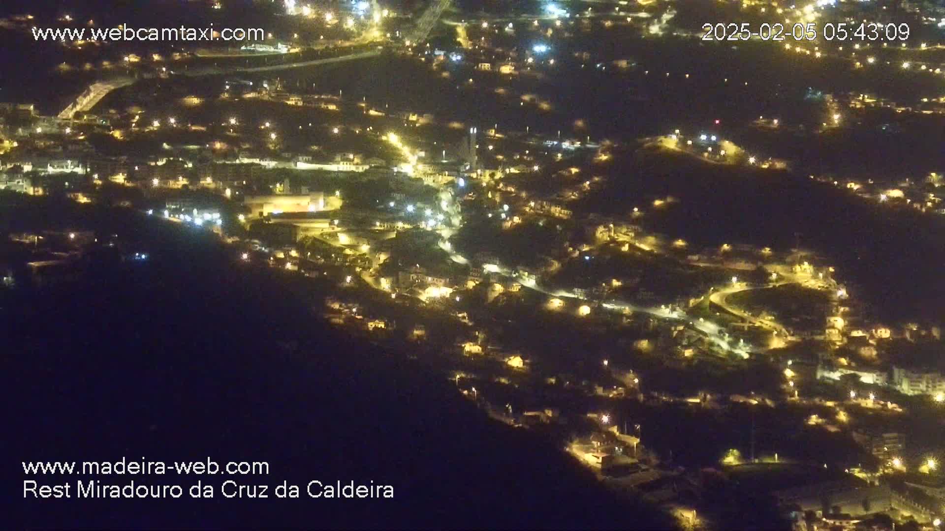 A nighttime aerial view shows a hillside town with many illuminated buildings and winding roads.