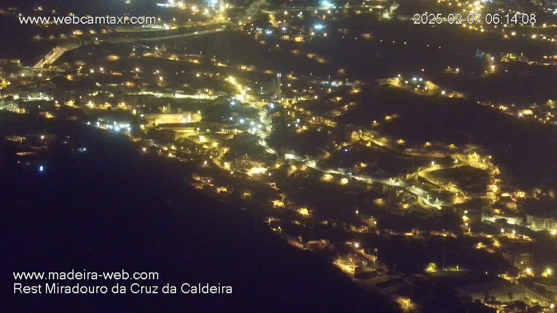 A nighttime, high-angle view of a town nestled on a hillside, illuminated by numerous lights.