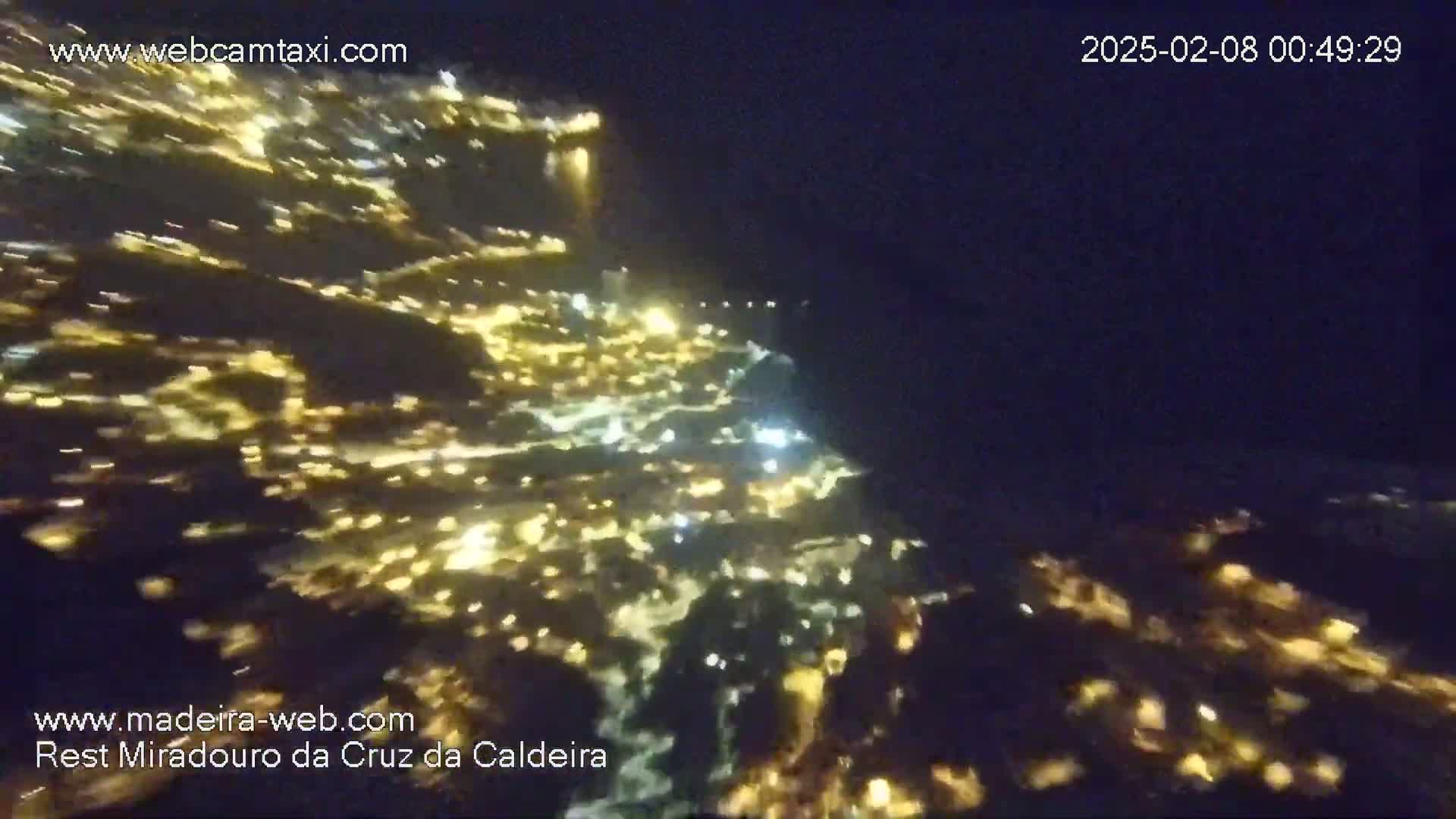 A nighttime aerial view shows a hillside town illuminated by many small, warm-toned lights.