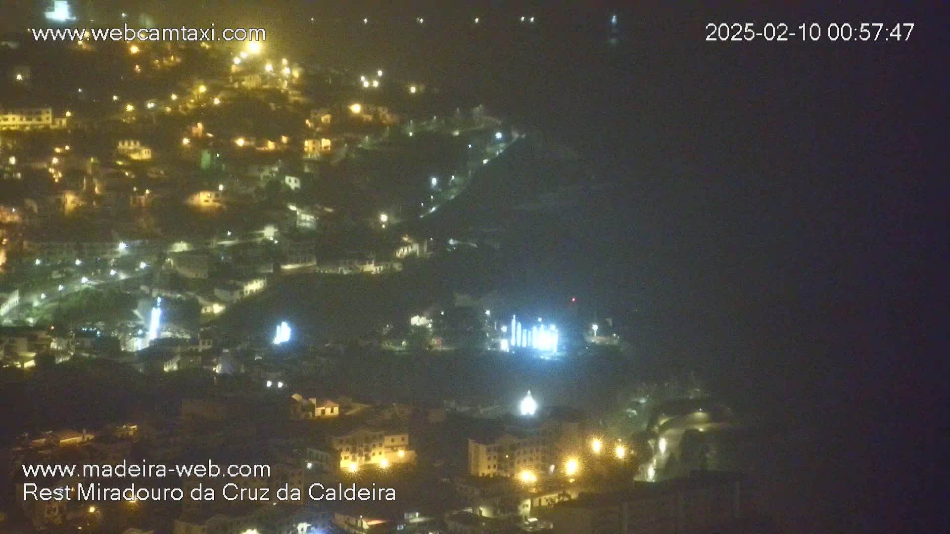 A nighttime, hazy view of a town nestled on a hillside, illuminated by scattered lights.