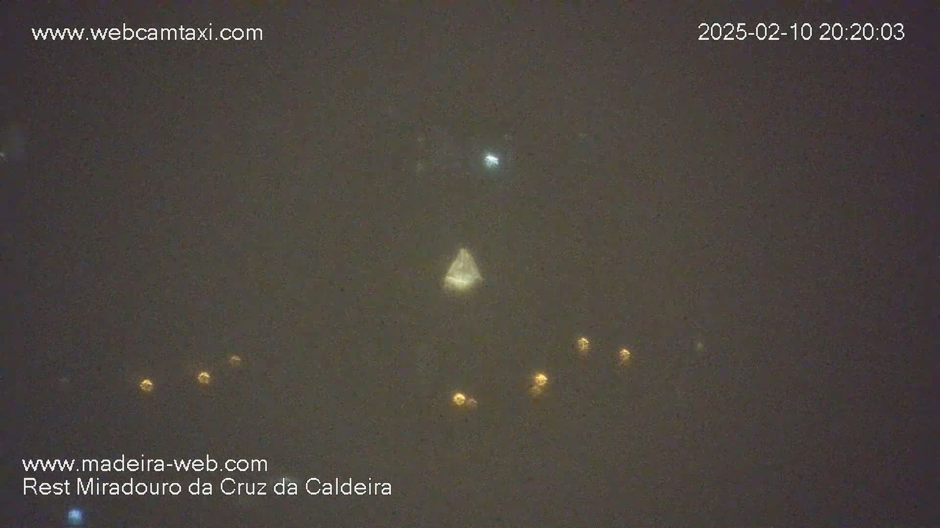 A nighttime, hazy scene shows several small, distant lights below a brighter, larger light in a triangular shape.