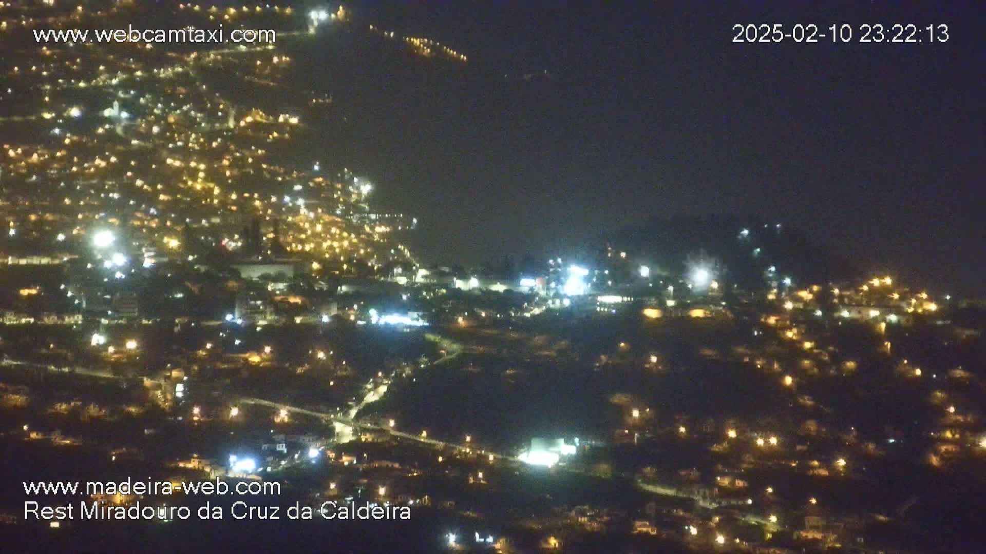 A nighttime, aerial view of a hillside city illuminated by numerous lights.