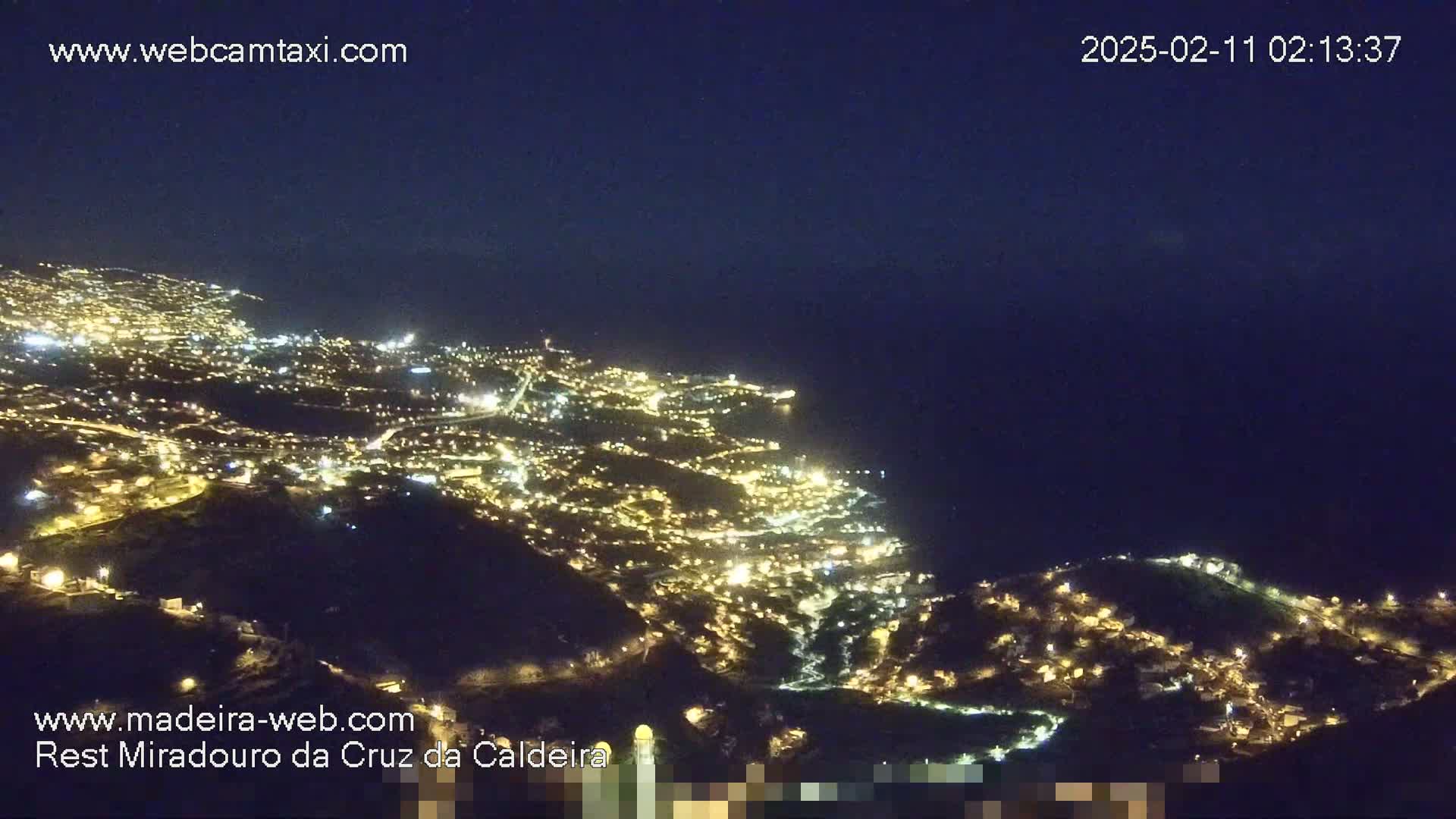 A nighttime, high-angle view shows a city illuminated by many lights along a coastline under a clear, dark sky.