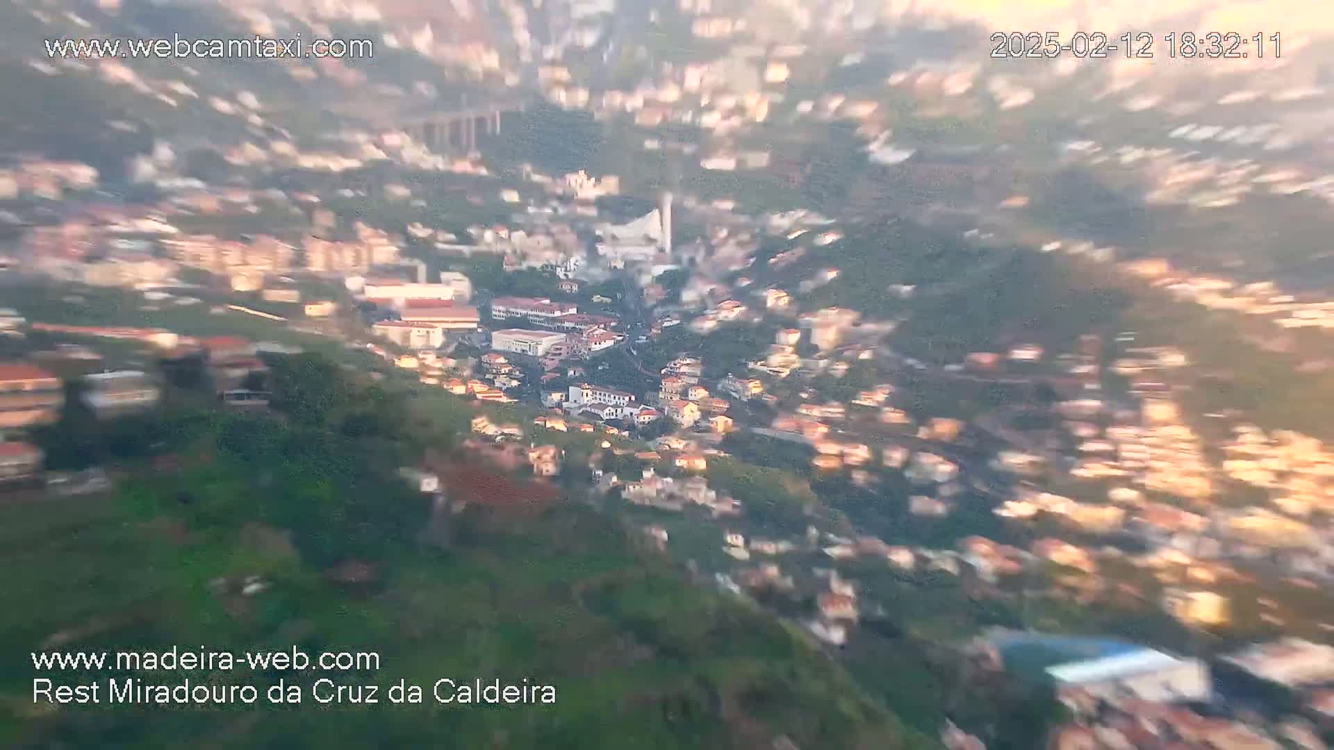 A blurry, high-angle, sunlit view shows a hillside town with many buildings.