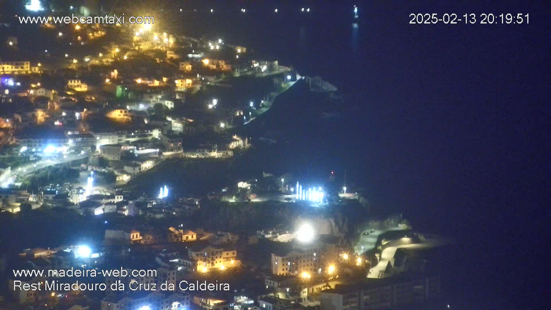 A nighttime, aerial view of a town built on a hillside overlooking a dark body of water.