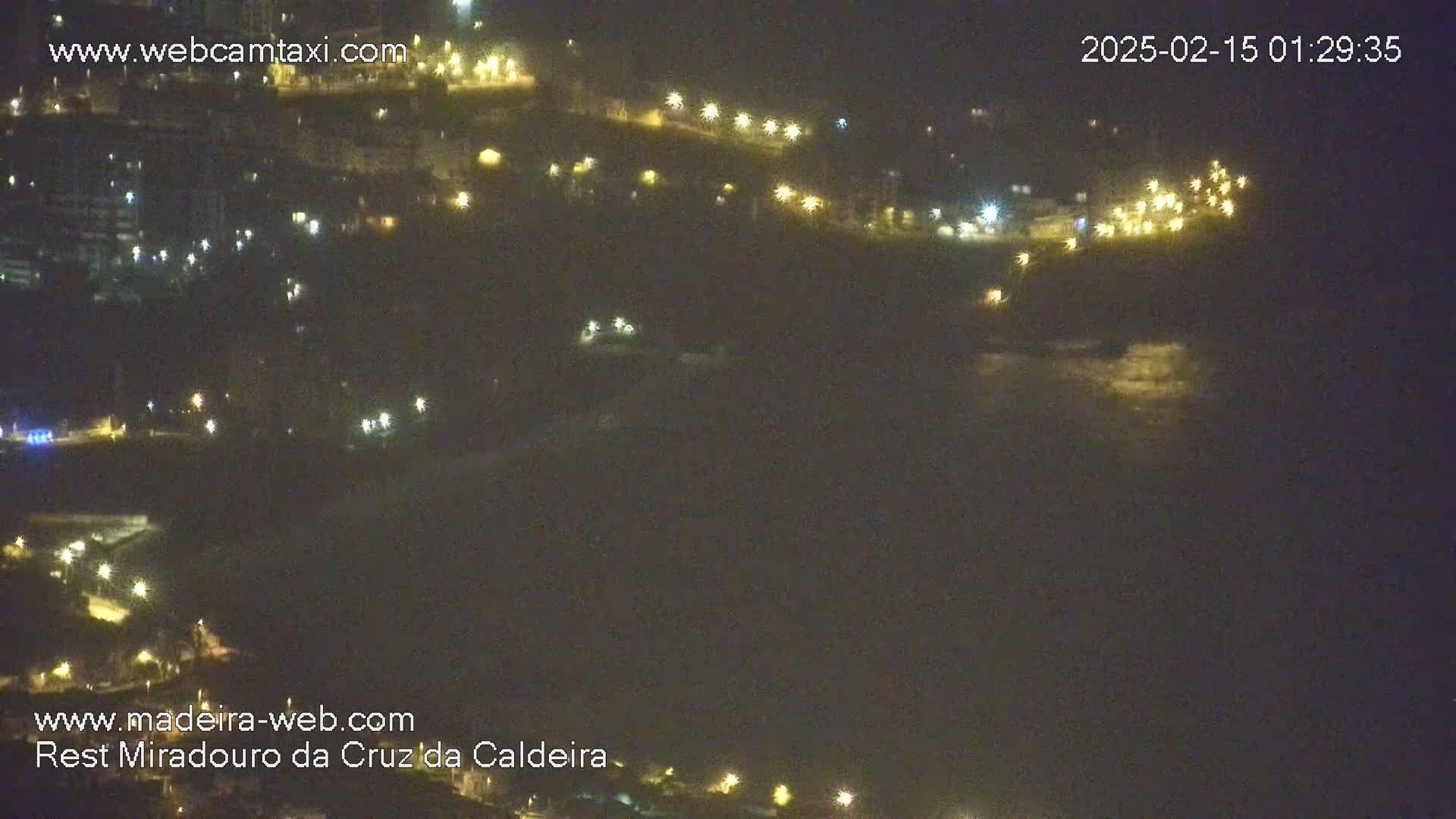 A nighttime, long shot of a hilly coastline with scattered lights and a dark ocean under a mostly clear sky.