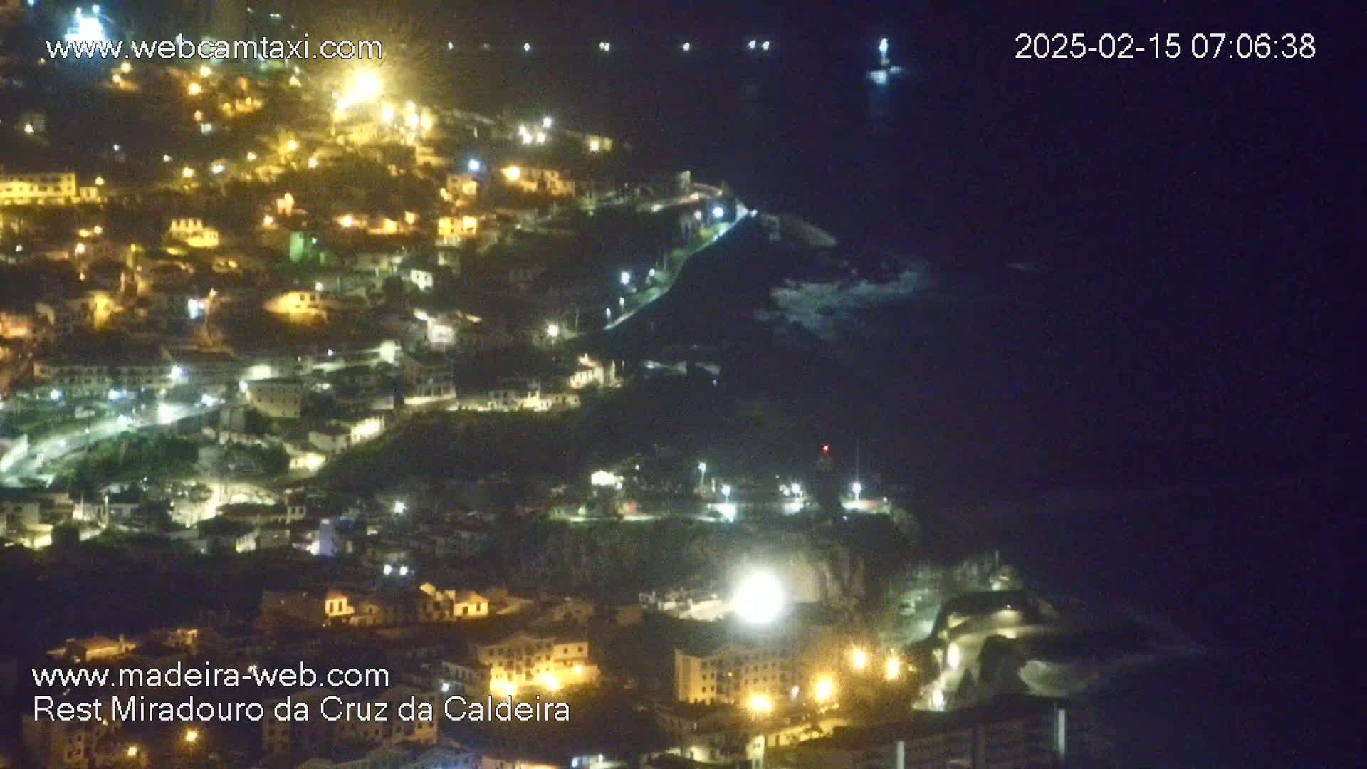 A nighttime, aerial view shows a coastal town illuminated by streetlights, overlooking a dark ocean.