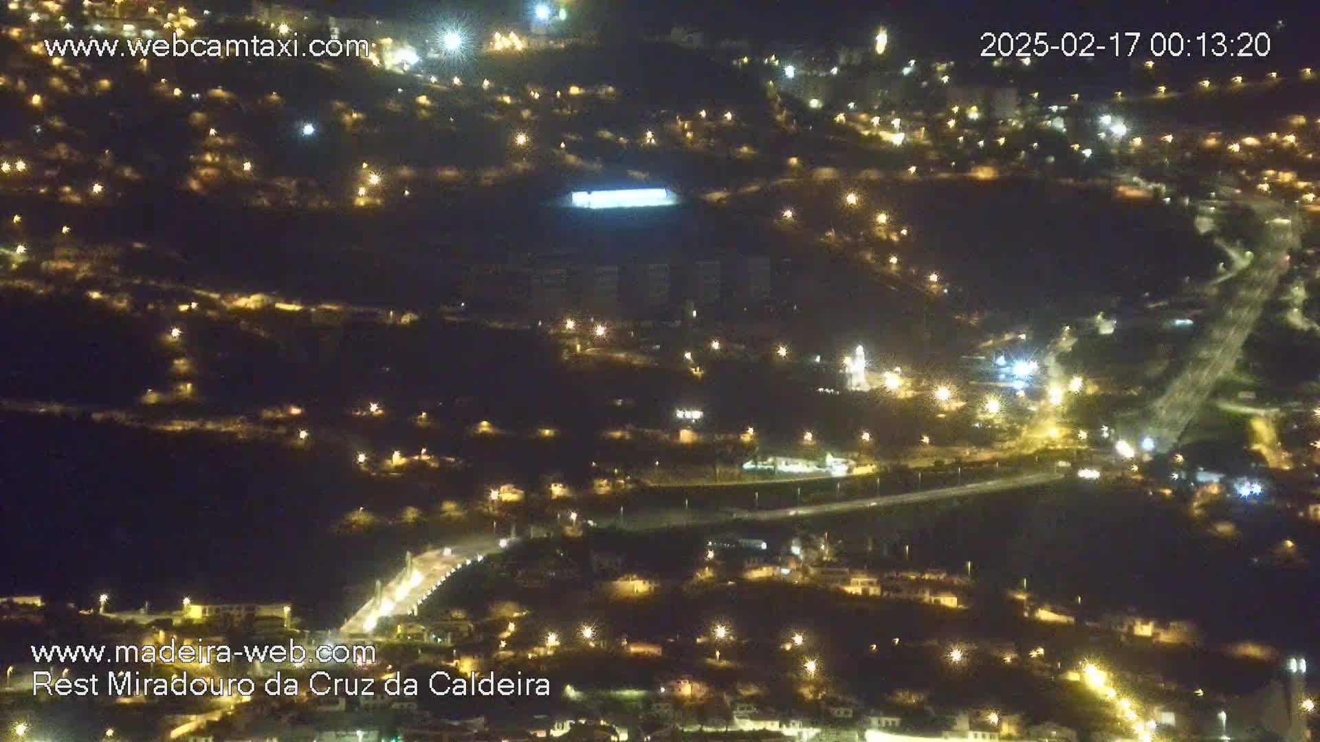 A nighttime aerial view of a town illuminated by numerous streetlights, with a road cutting through it.