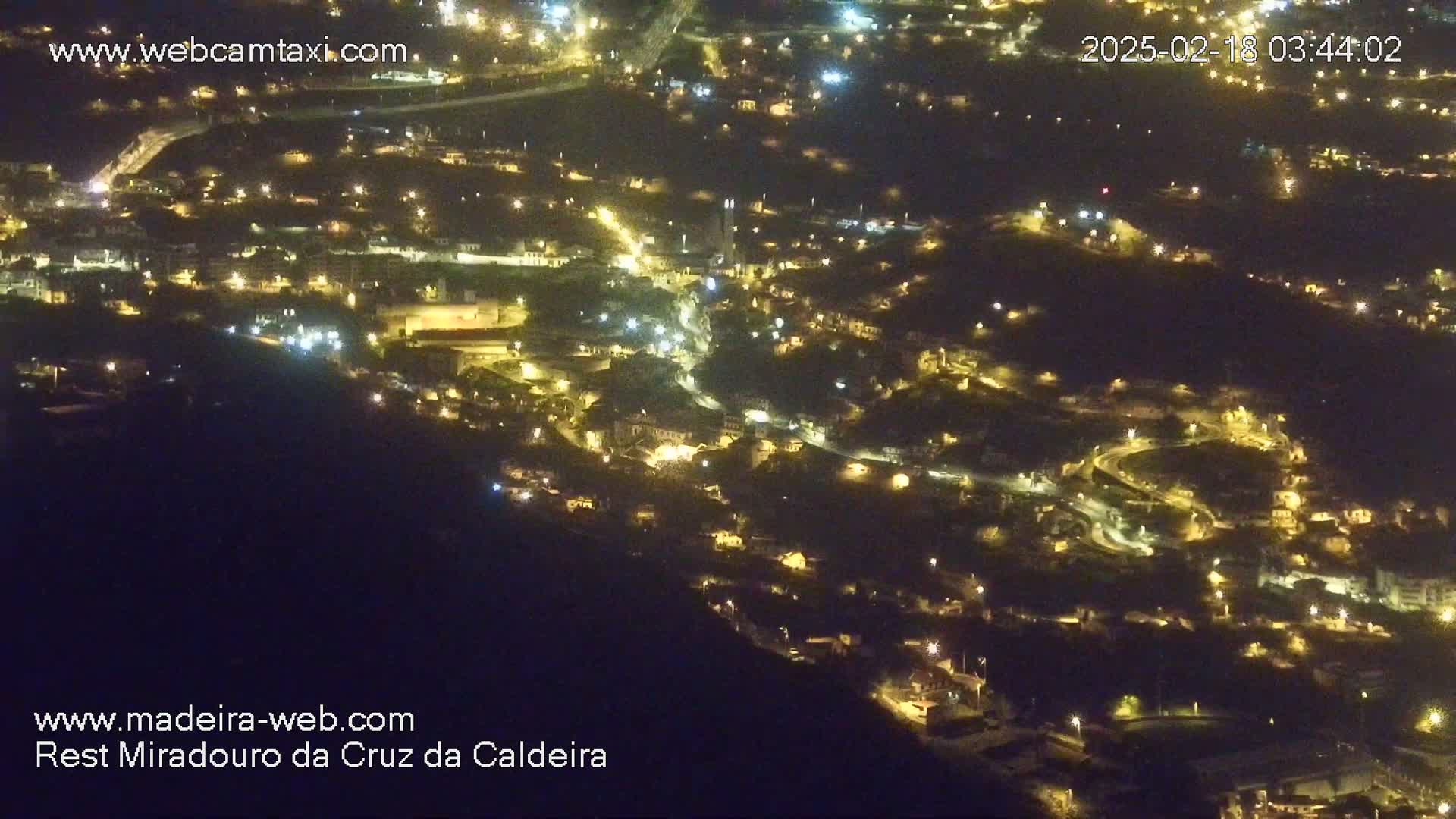 A nighttime aerial view shows a hillside town illuminated by many small lights.