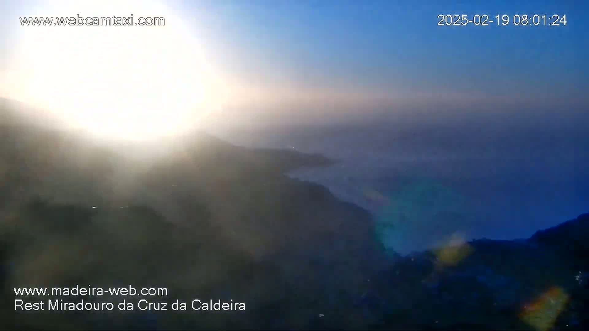 A hazy sunrise over a mountainous landscape with low-lying clouds or fog in the distance.