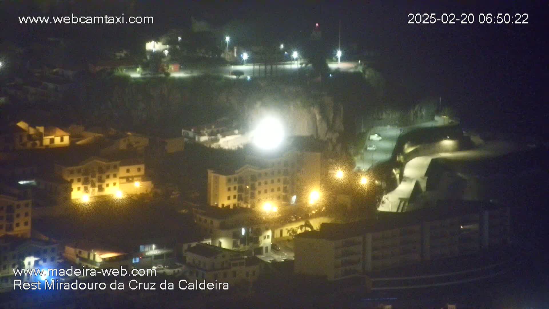 A nighttime, high-angle view of a coastal town illuminated by streetlights, situated on a cliffside.