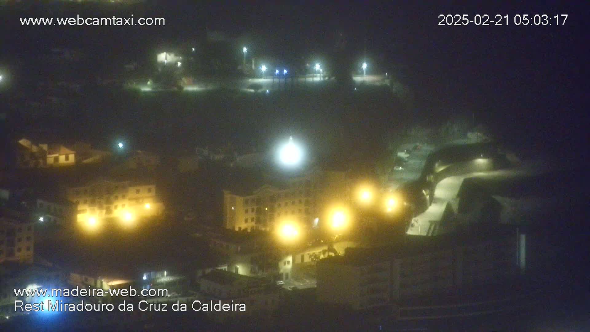 A nighttime, hazy view of a town with illuminated buildings and streetlights.