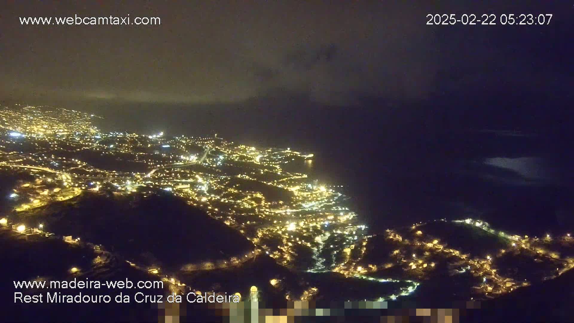 A nighttime aerial view shows a coastal city illuminated with many small lights, overlooking a dark ocean under a mostly clear sky.