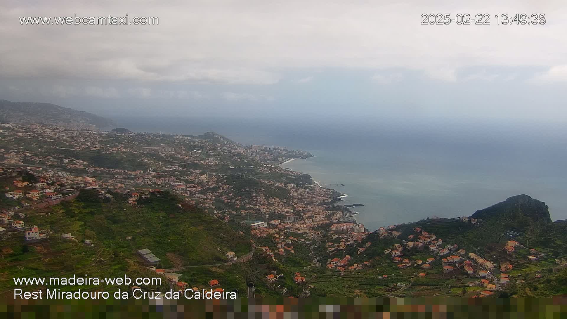 A coastal town nestled on a hillside overlooking the ocean under an overcast sky.