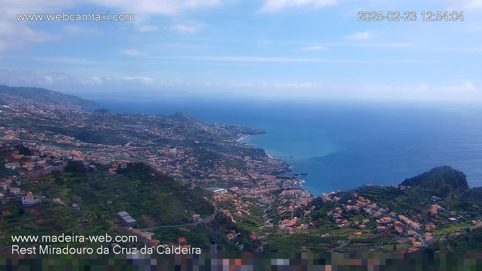 A coastal town nestled on a hillside overlooking a calm ocean under a mostly clear sky.