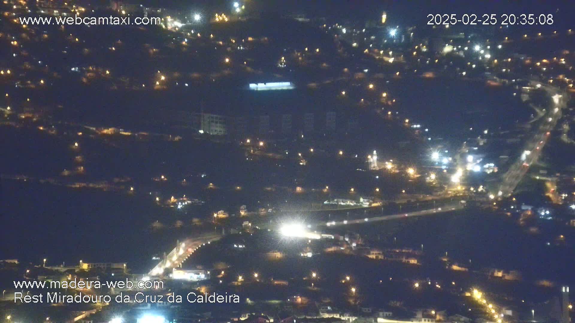 A nighttime, high-angle view of a town illuminated by scattered streetlights and car headlights along roads.