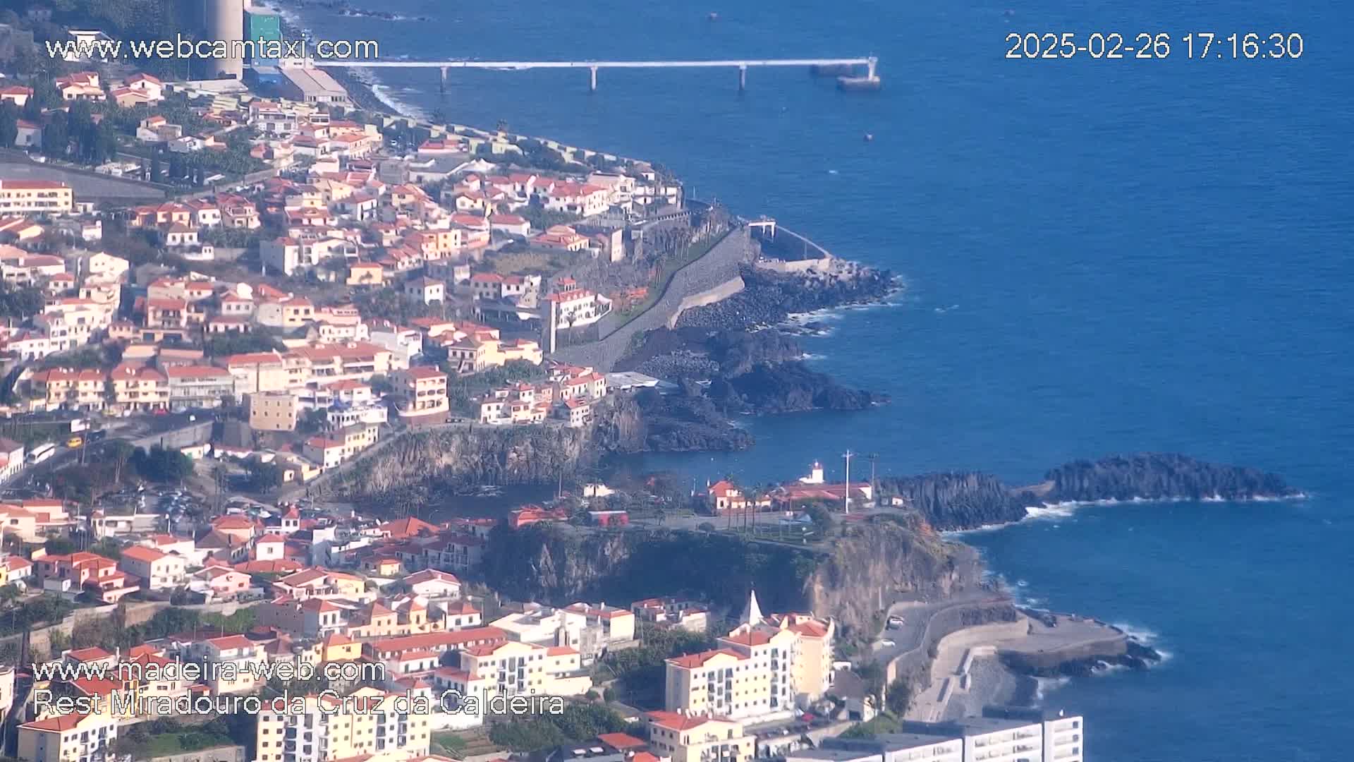 A coastal town with many low-rise buildings sits on a cliff overlooking a dark blue ocean on a clear day.