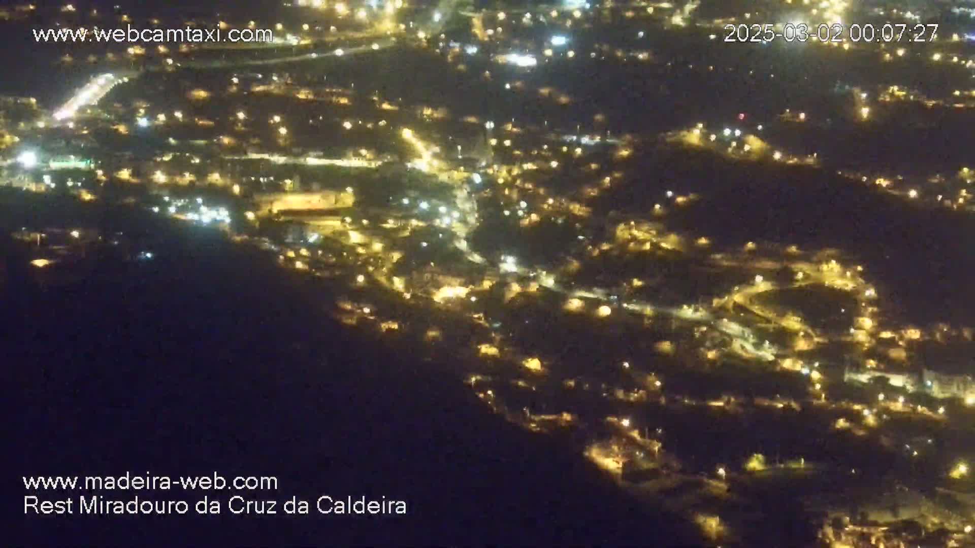 A nighttime, high-angle view shows a sprawling town illuminated by numerous lights spread across a hillside.