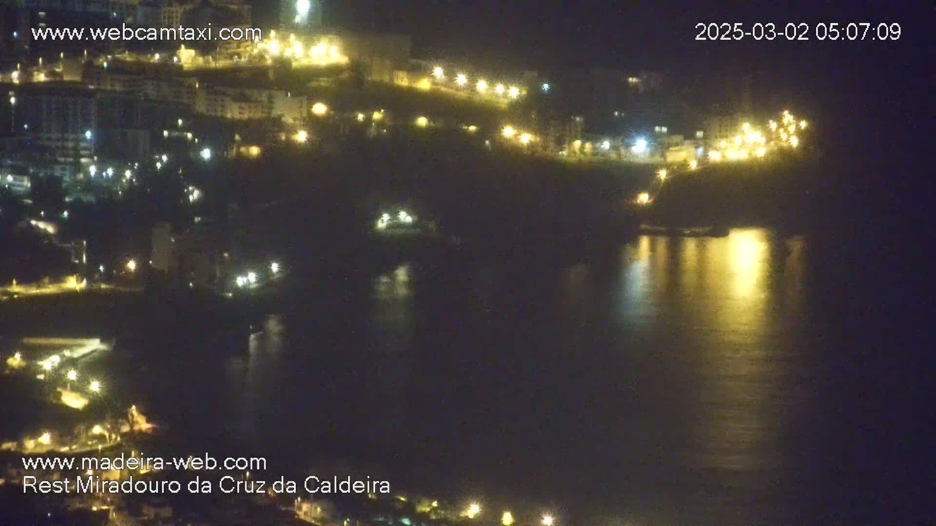 A nighttime view of a coastal town with lights reflecting on calm water.