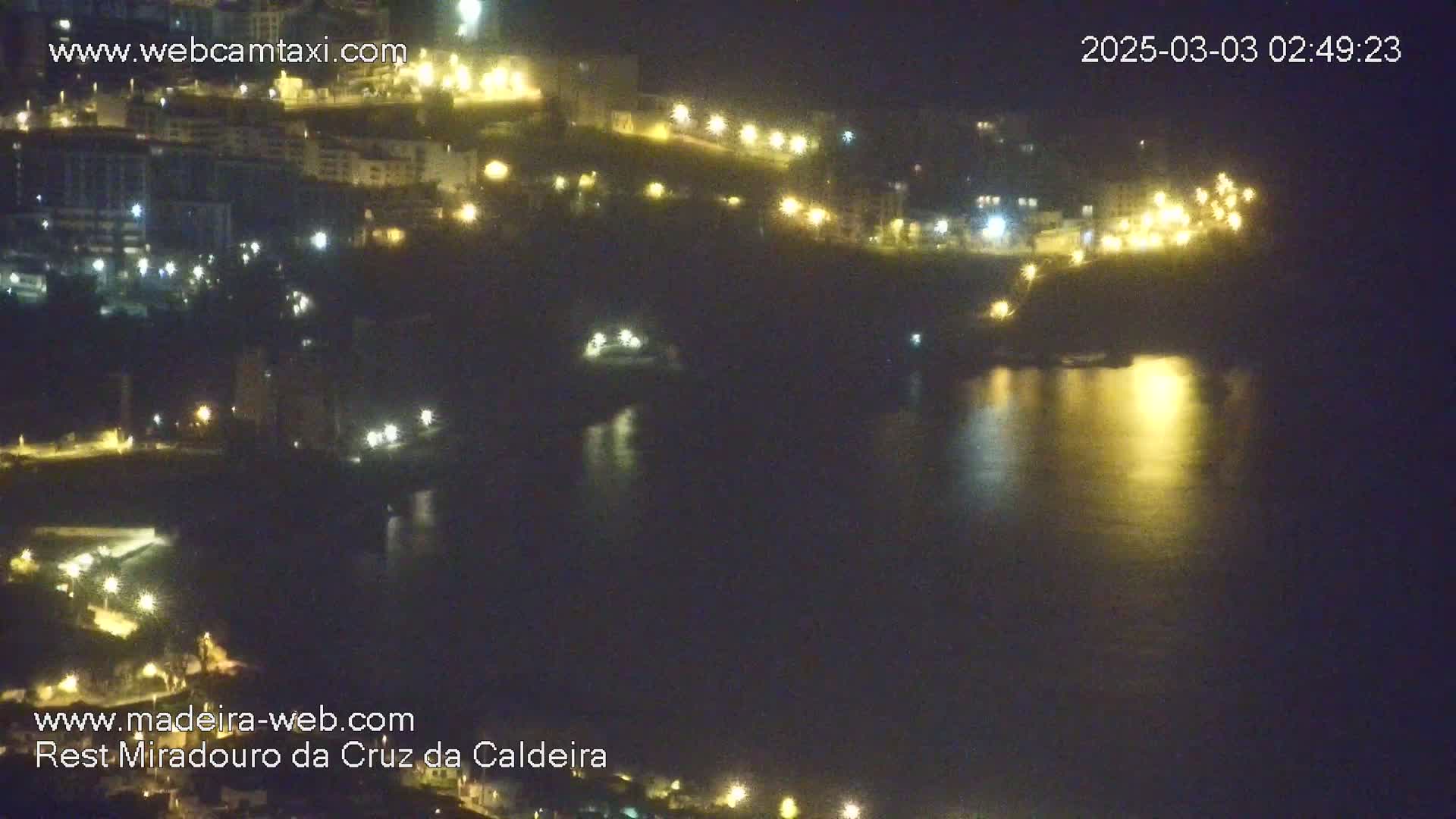 A nighttime view of a calm body of water reflecting the lights of a town on a hillside.