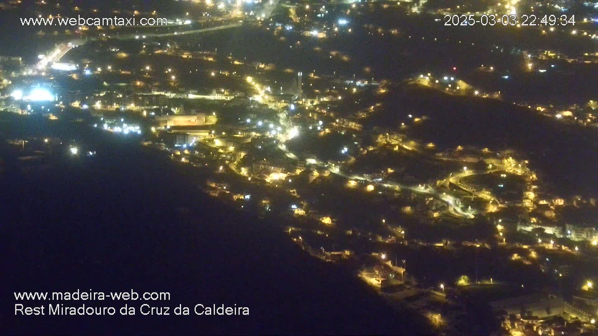 A nighttime, high-angle view of a town nestled in a hilly landscape, illuminated by scattered lights.