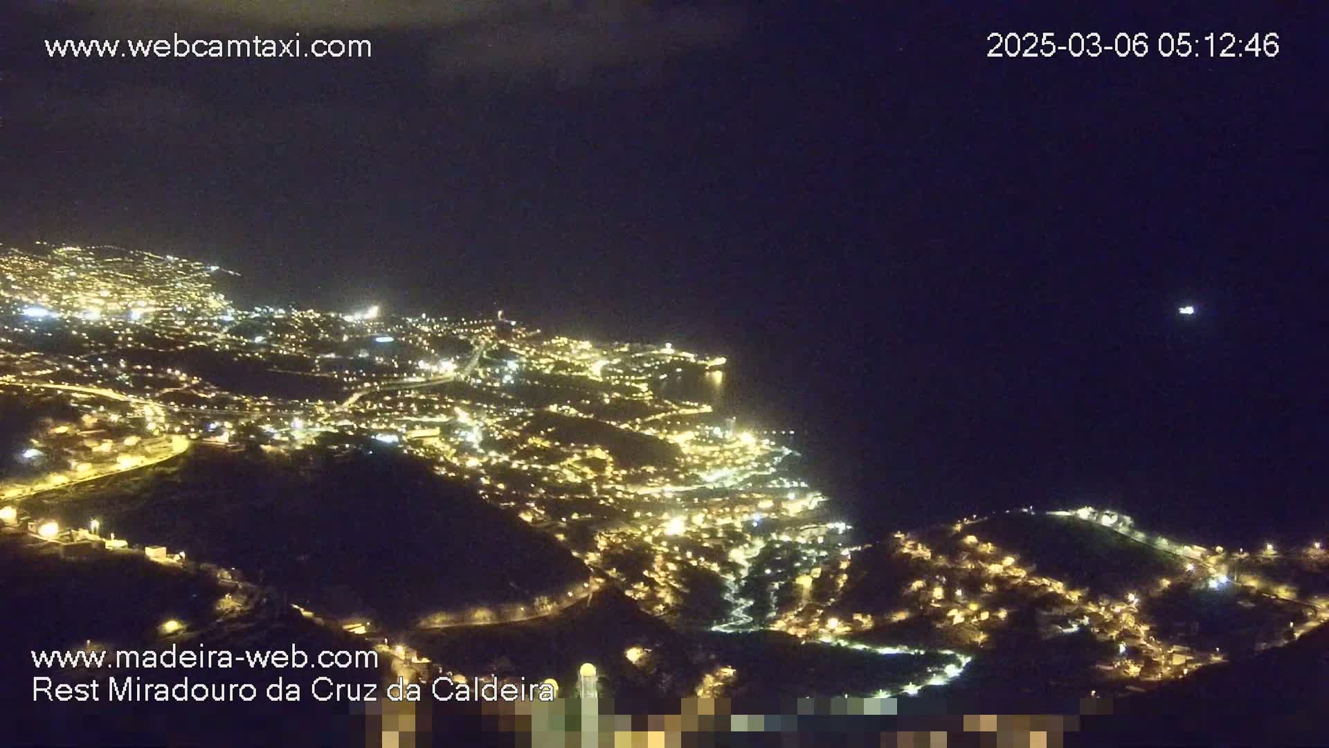 A nighttime, aerial view shows a city illuminated by many lights stretching along a dark coastline under a clear, dark sky.