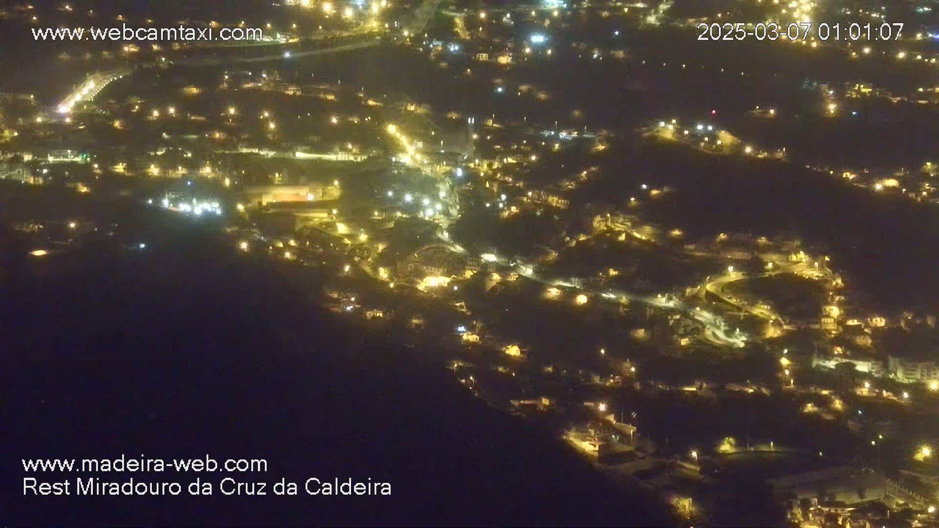 A nighttime, high-angle view shows a hillside town illuminated by many small lights.