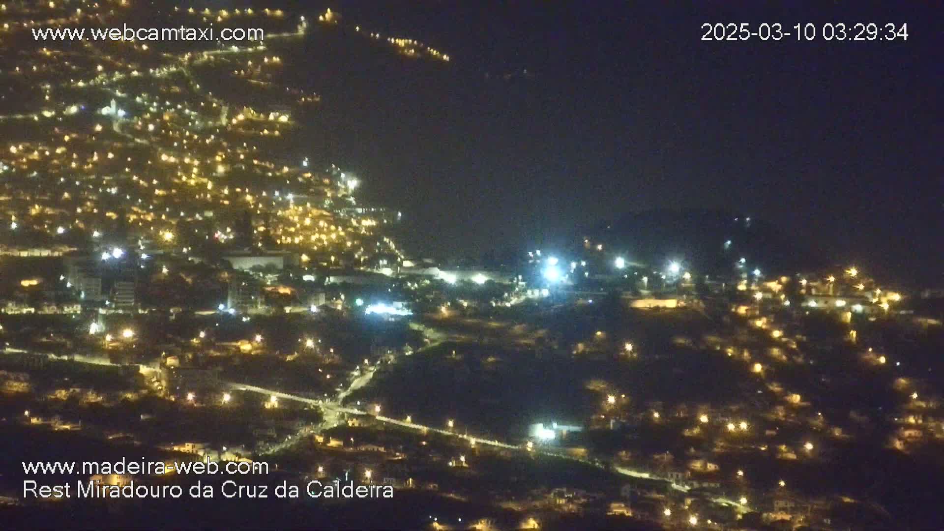 A nighttime, aerial view of a hillside town illuminated by numerous lights.