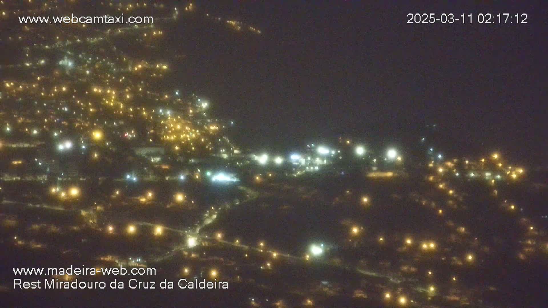 A nighttime aerial view of a town illuminated by scattered lights, under a dark, hazy sky.