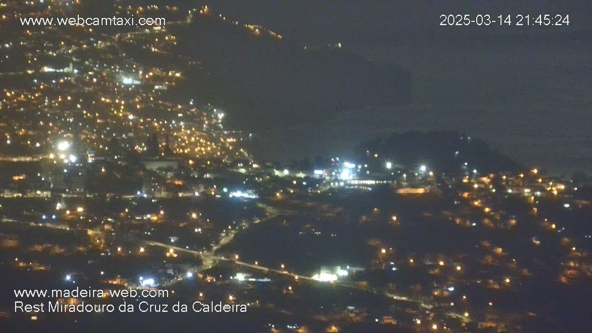 A nighttime, aerial view of a city illuminated by numerous streetlights, with dark hills or mountains visible in the background under a clear, dark sky.