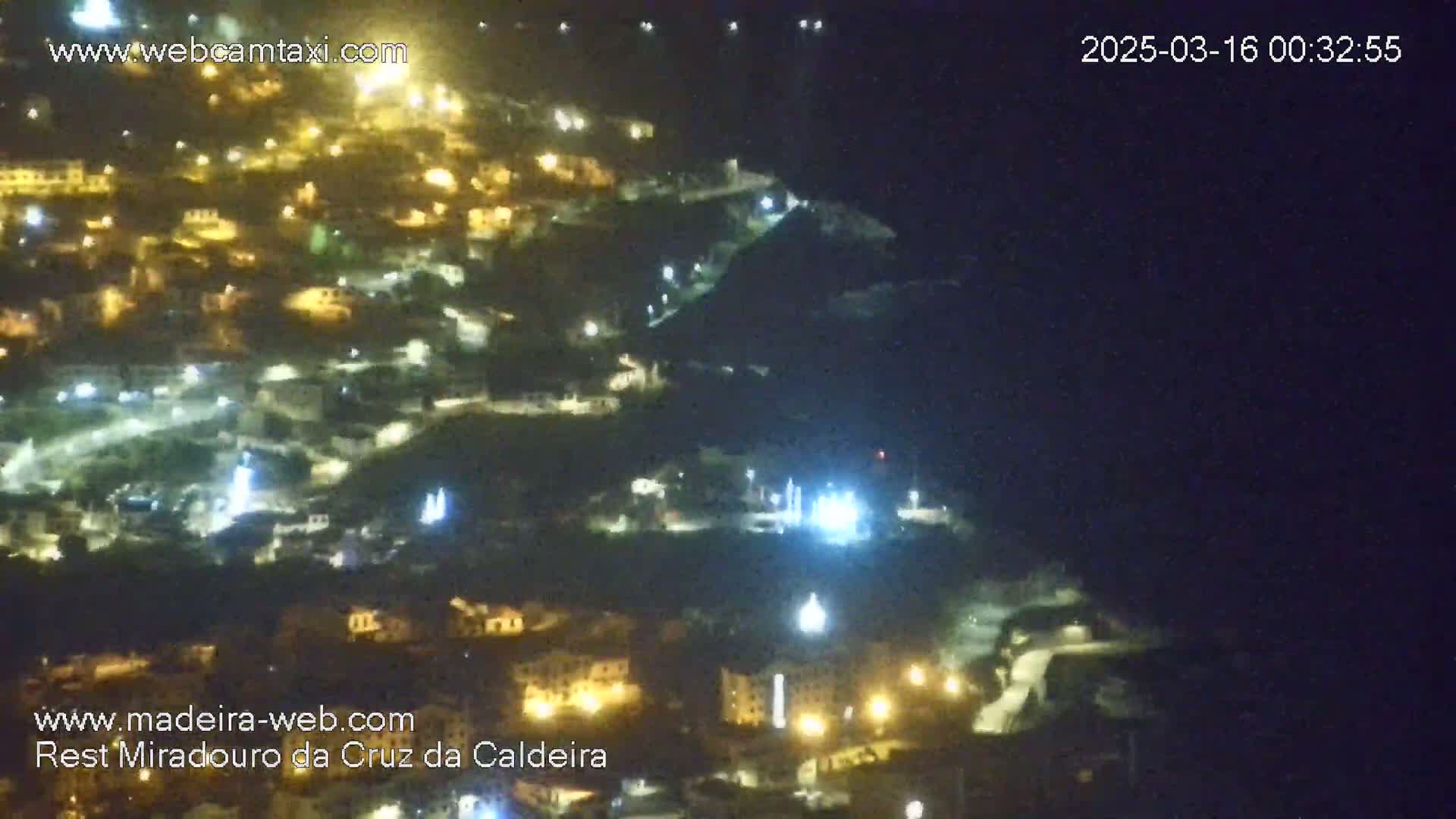 A nighttime, high-angle view shows a hillside village illuminated by numerous lights.