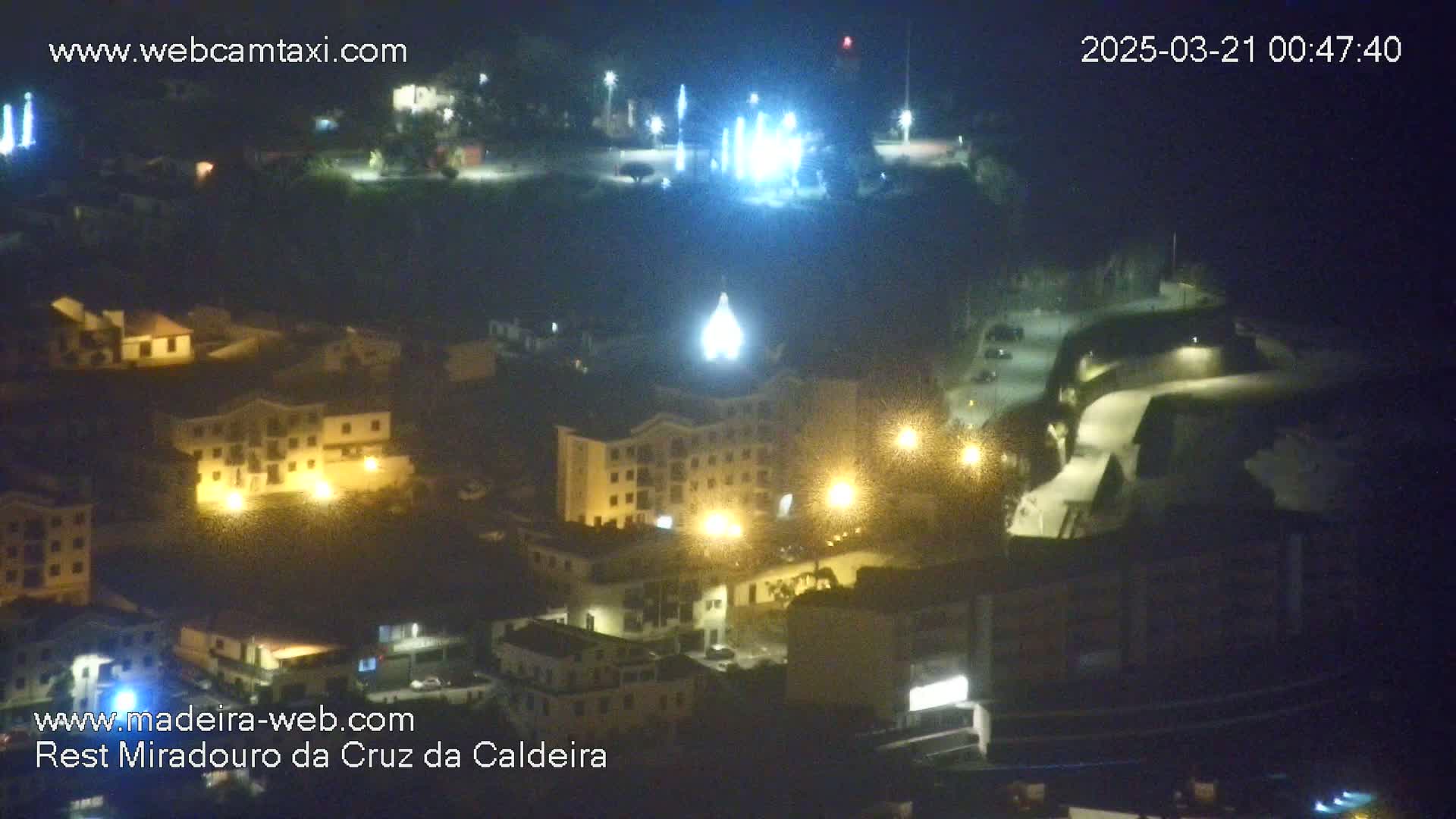 A nighttime, high-angle view of a town with illuminated buildings, streets, and some distant lights.