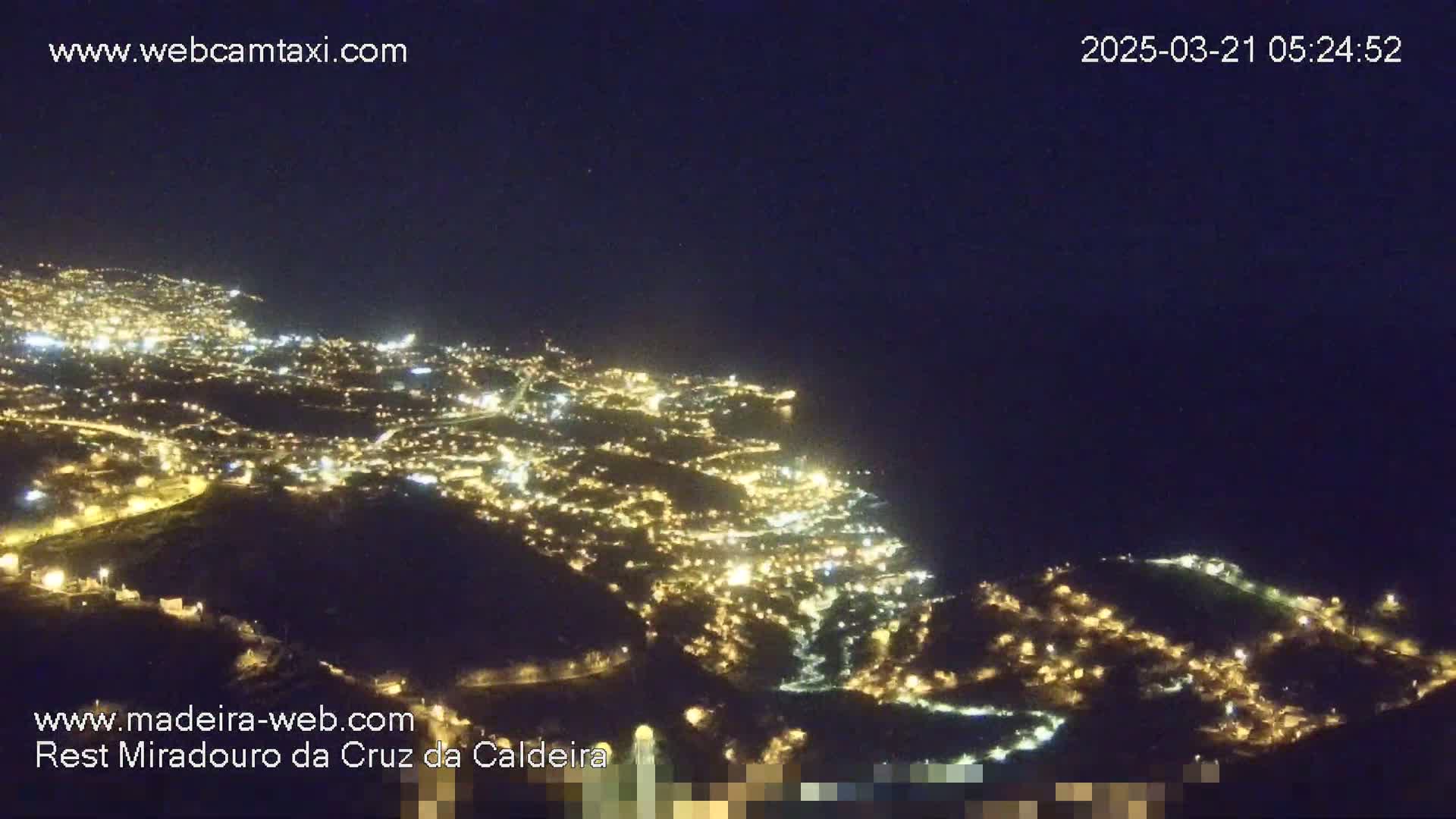 A nighttime aerial view shows a city illuminated by many lights along a dark coastline under a clear, dark sky.