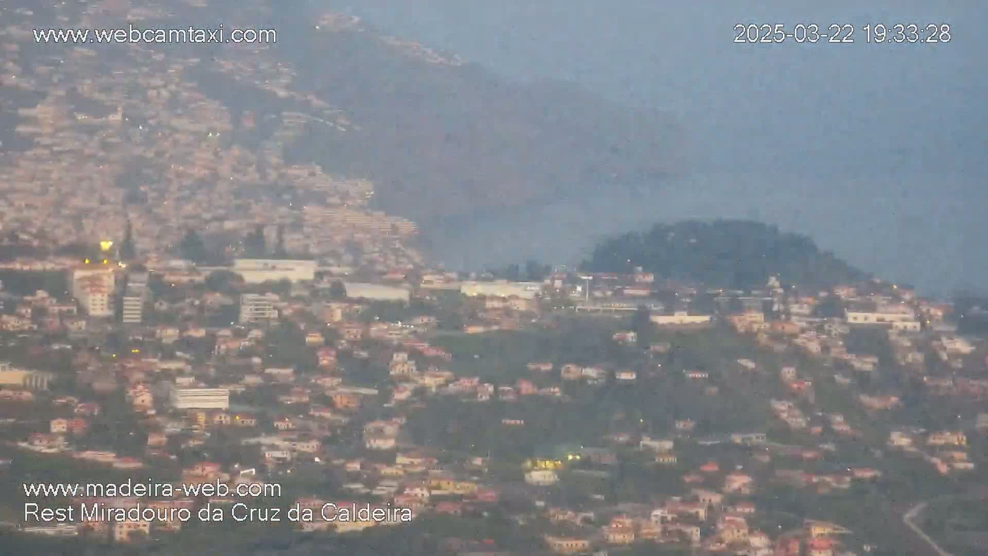 A hazy, dusk view shows a sprawling city built on hillsides and mountains.