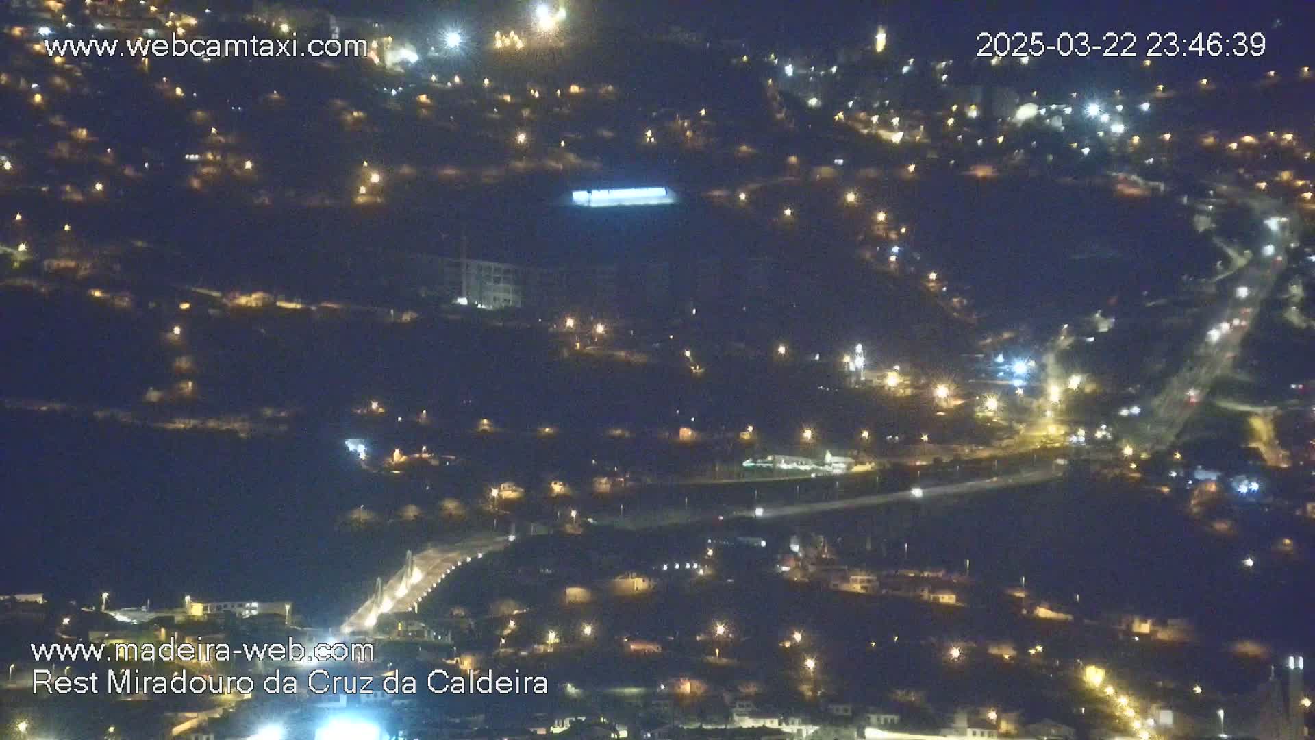 A nighttime aerial view shows a hillside town illuminated by numerous streetlights.