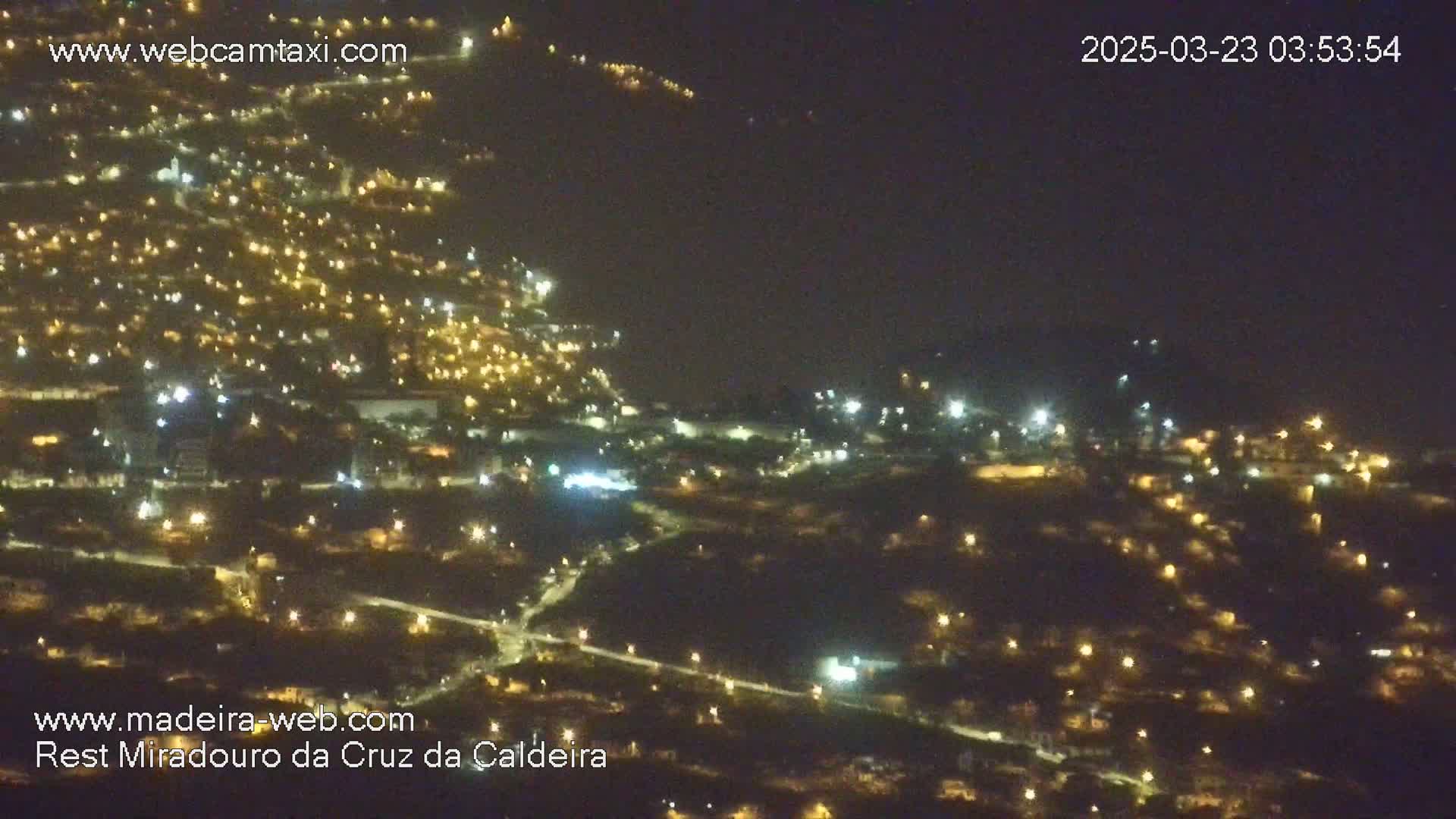 A nighttime, high-angle view of a town illuminated by numerous lights spread across a hilly landscape.