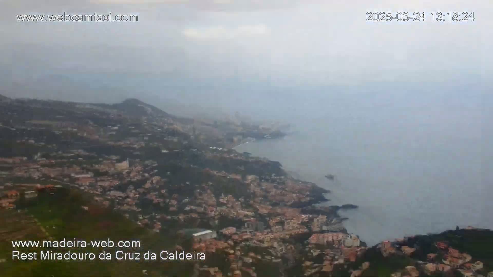 A hazy, distant view of a coastal city sprawling down a hillside to meet a calm ocean.