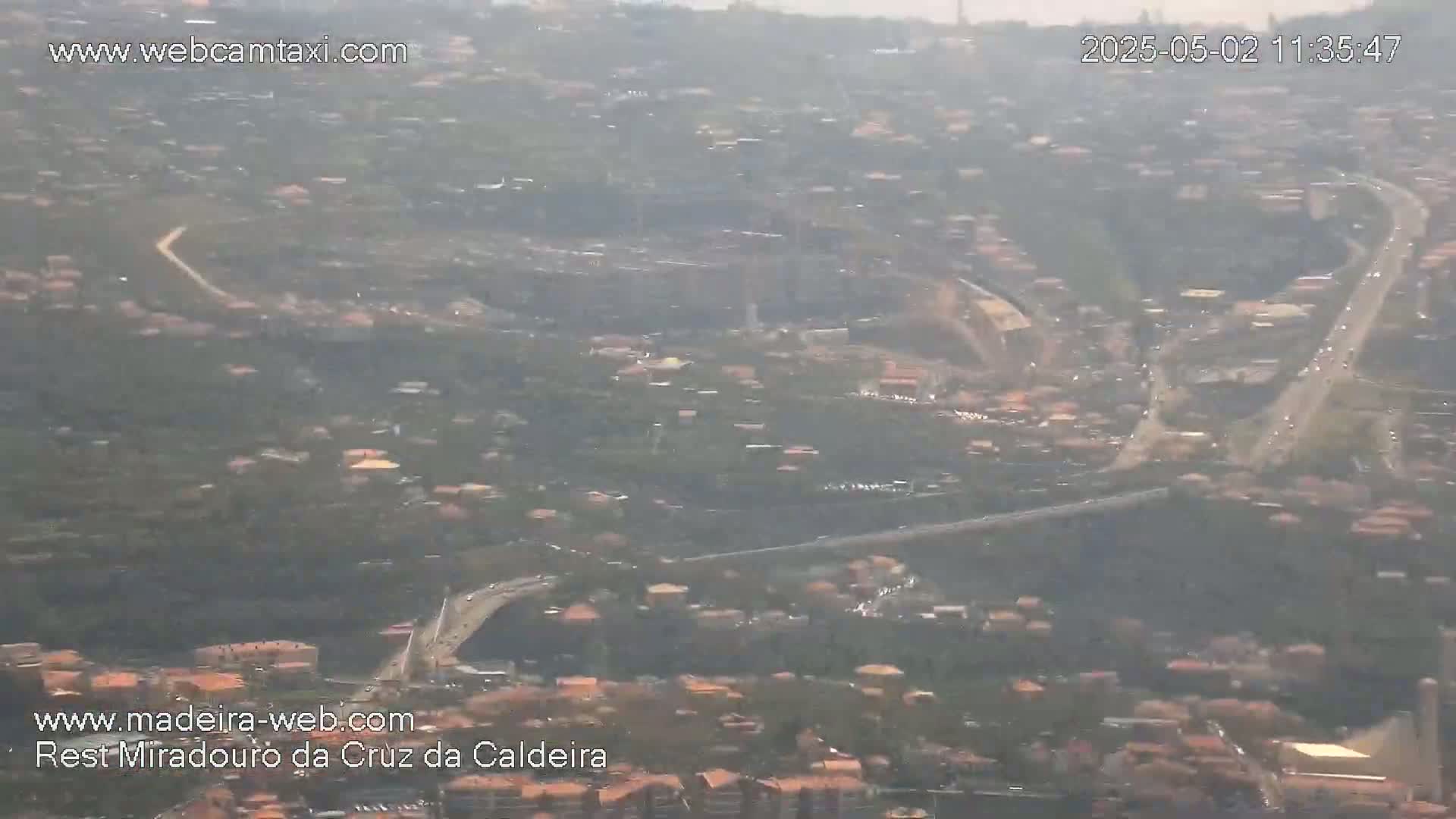 A hazy, high-angle view shows a sprawling town with winding roads and sparse vegetation.
