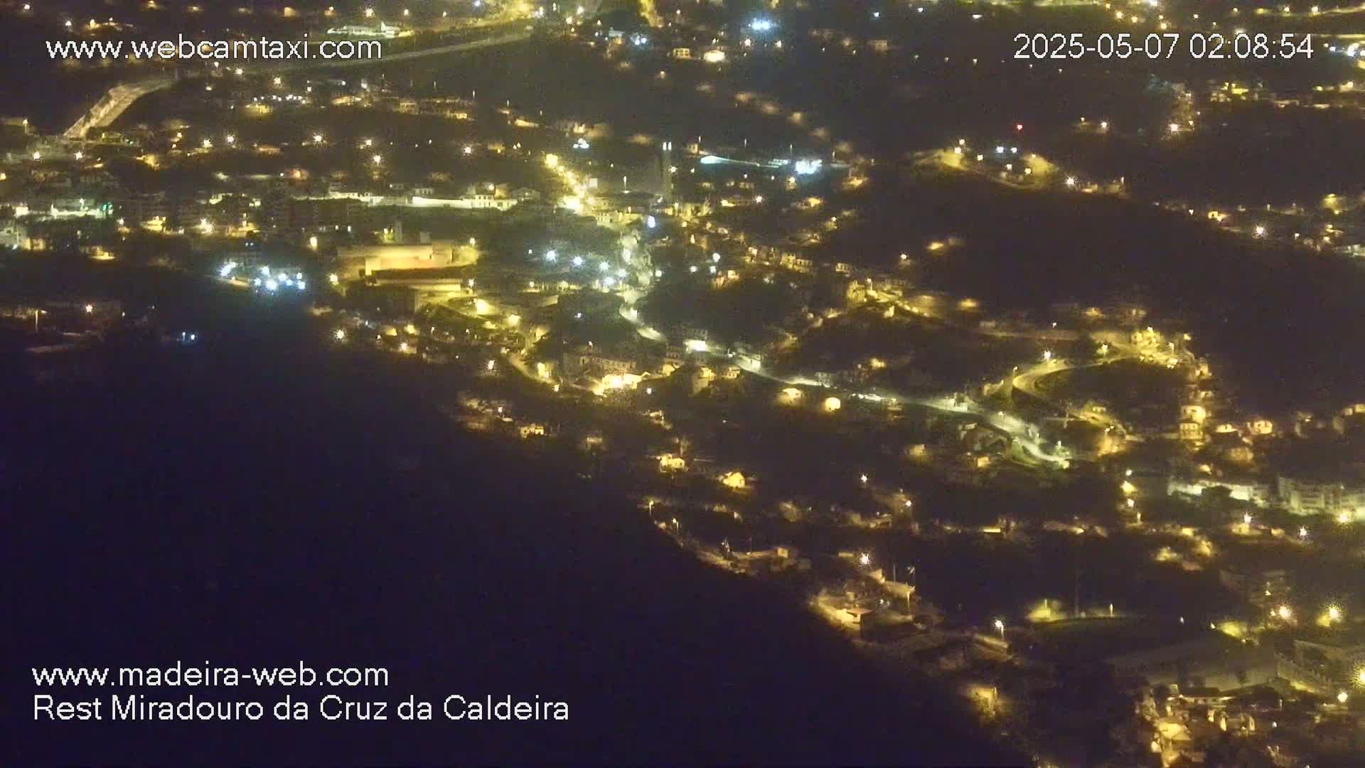 A nighttime, high-angle view shows a hillside town illuminated by many small lights.