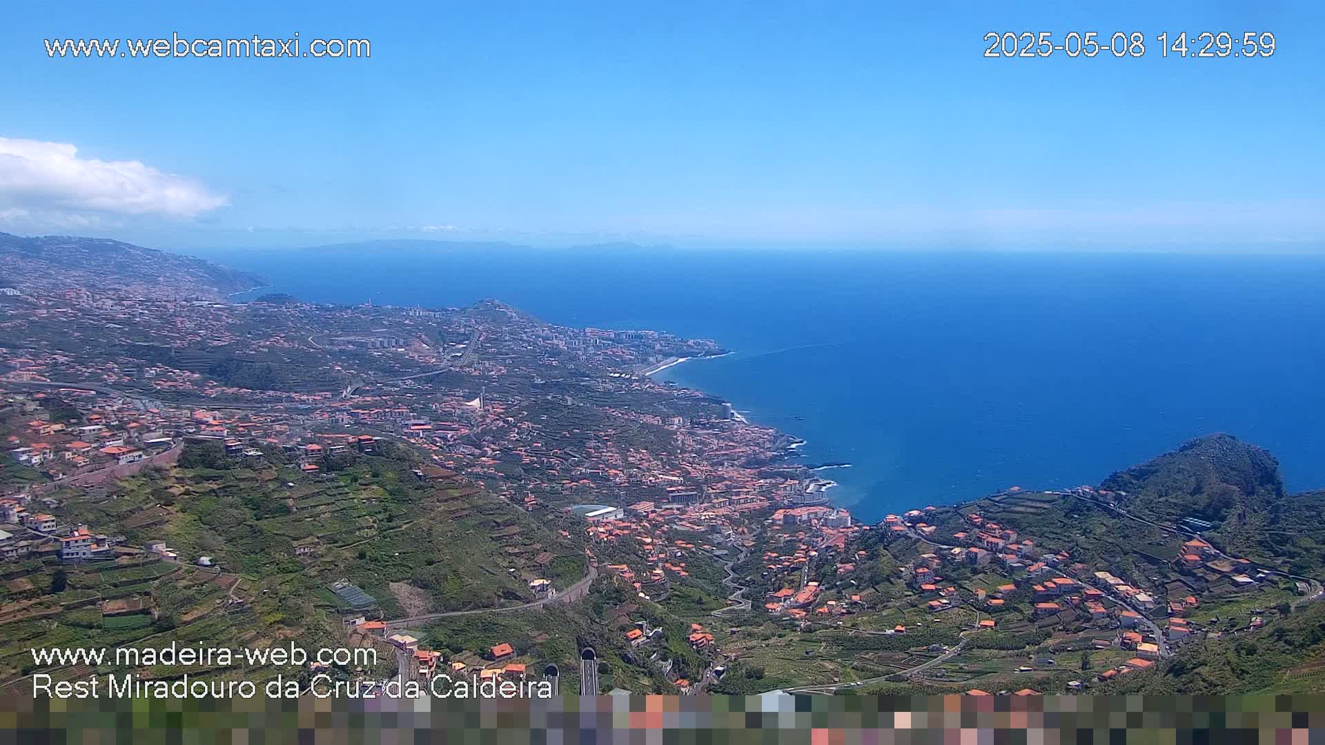 A coastal town with terraced hillsides descends to a blue ocean under a clear sky.